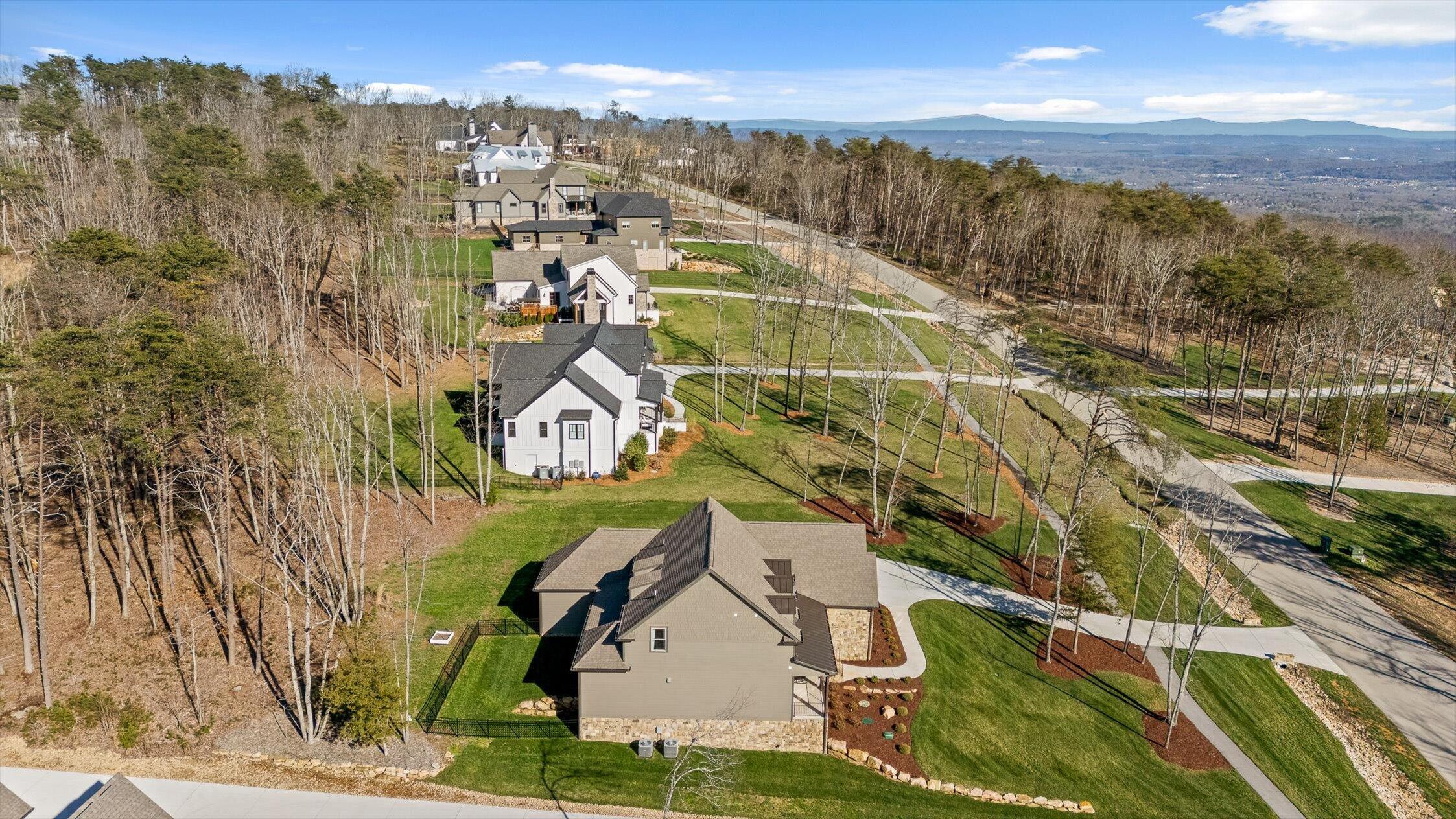 Aerial view of a home among wooded lots, with curving roads and distant mountain ridges.