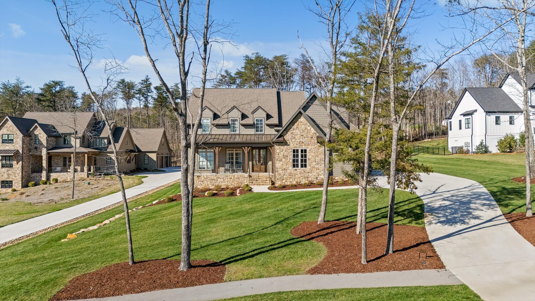 Stone-and-siding home with a covered porch, landscaped lawn, and curved driveway.