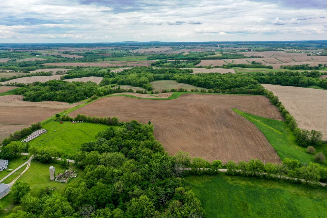 Aerial view of rolling farmland with broad fields, tree lines, and scattered farm buildings.