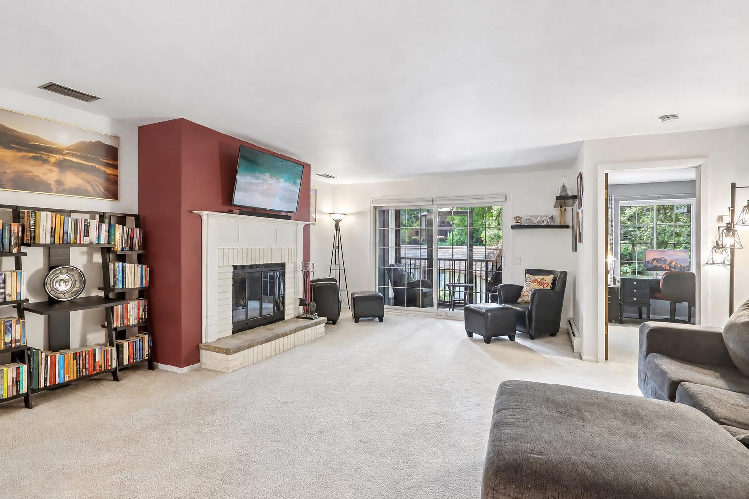 Living room with a white brick fireplace, built-in bookshelves, and sliding glass doors to a leafy patio.