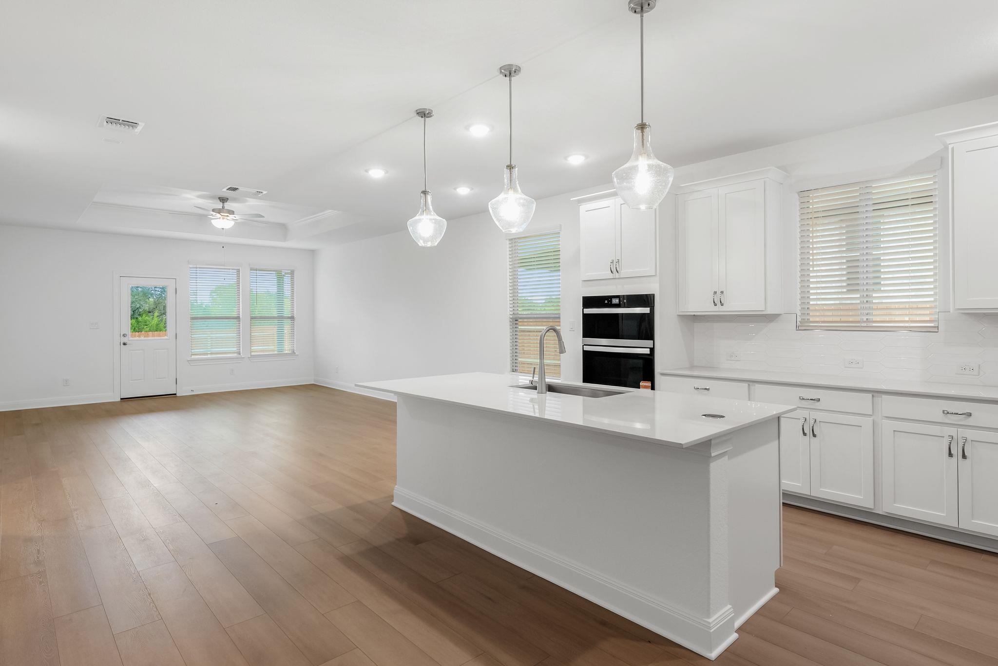 Open kitchen with a large white island, pendant lights, and double wall ovens.