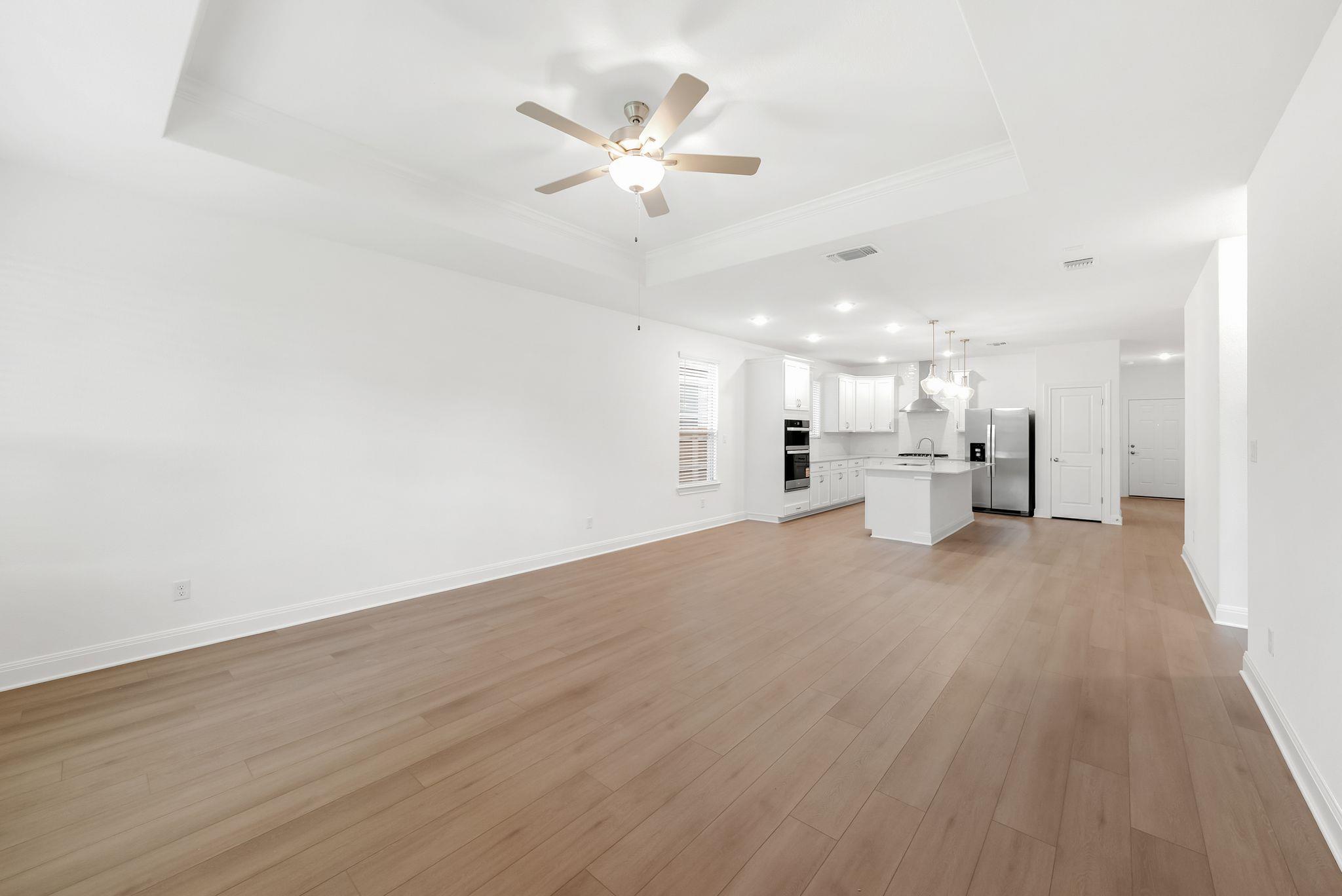 Open-plan living area and kitchen with light wood floors, white cabinets, and stainless steel appliances.