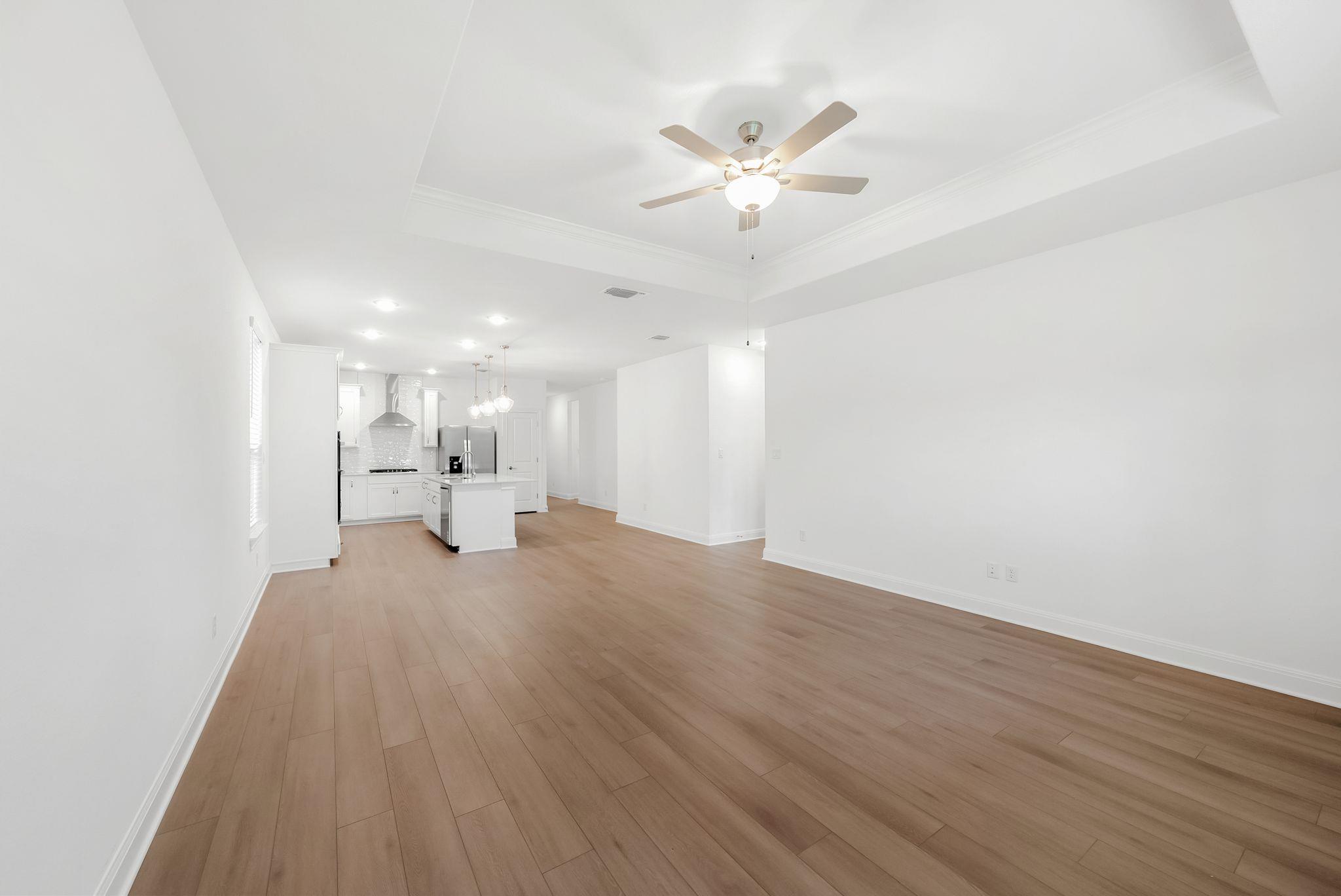 Empty open-plan living area with wood flooring, a white kitchen island, and a tray ceiling fan.