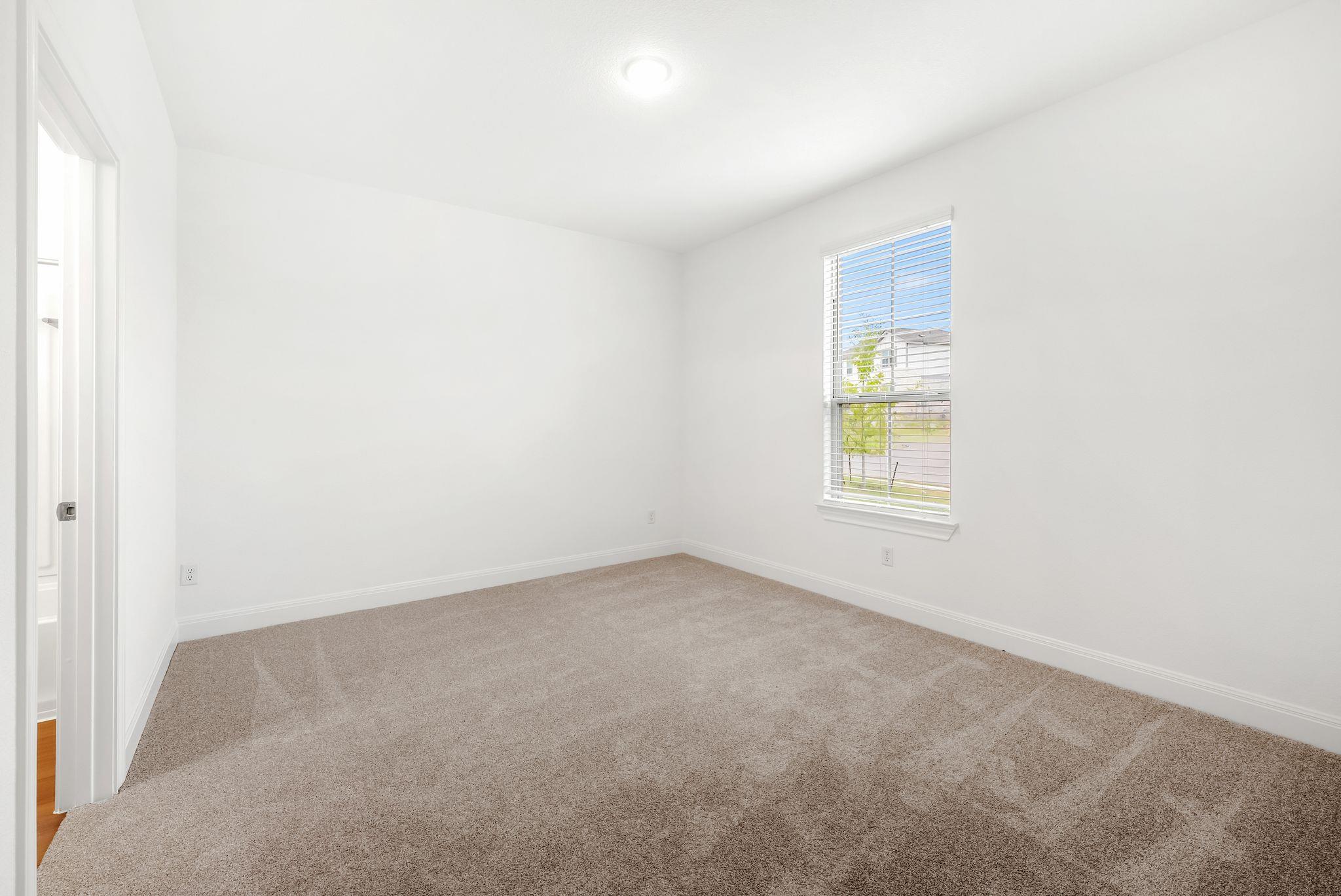 Empty bedroom with beige carpet and a window fitted with white blinds.