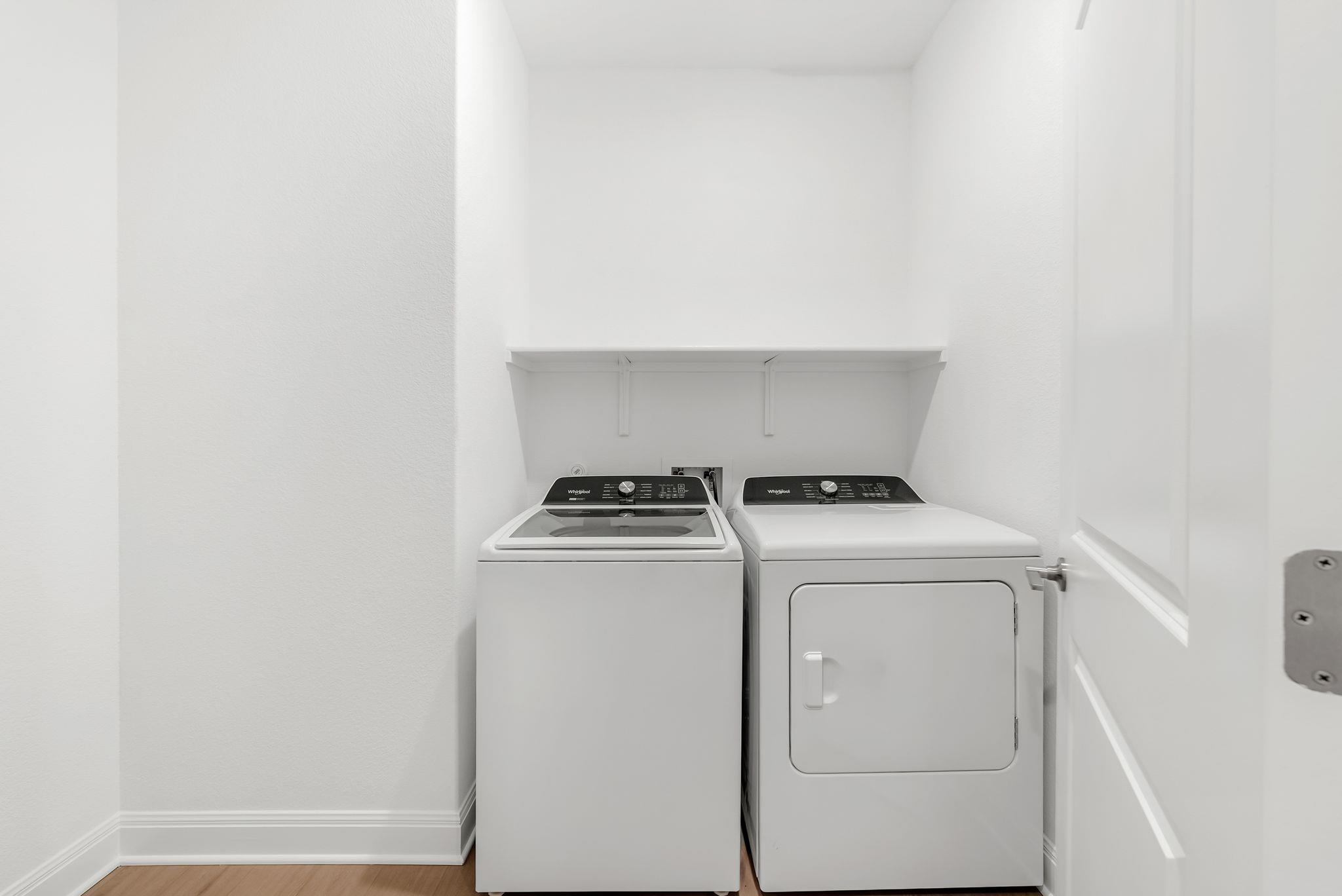 Laundry room with a white washer and dryer beneath a wall shelf.