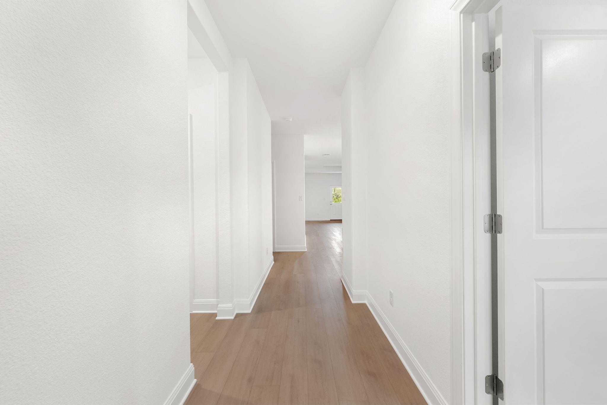 Vacant hallway with light wood-look floors, white walls, and an open doorway at the far end.