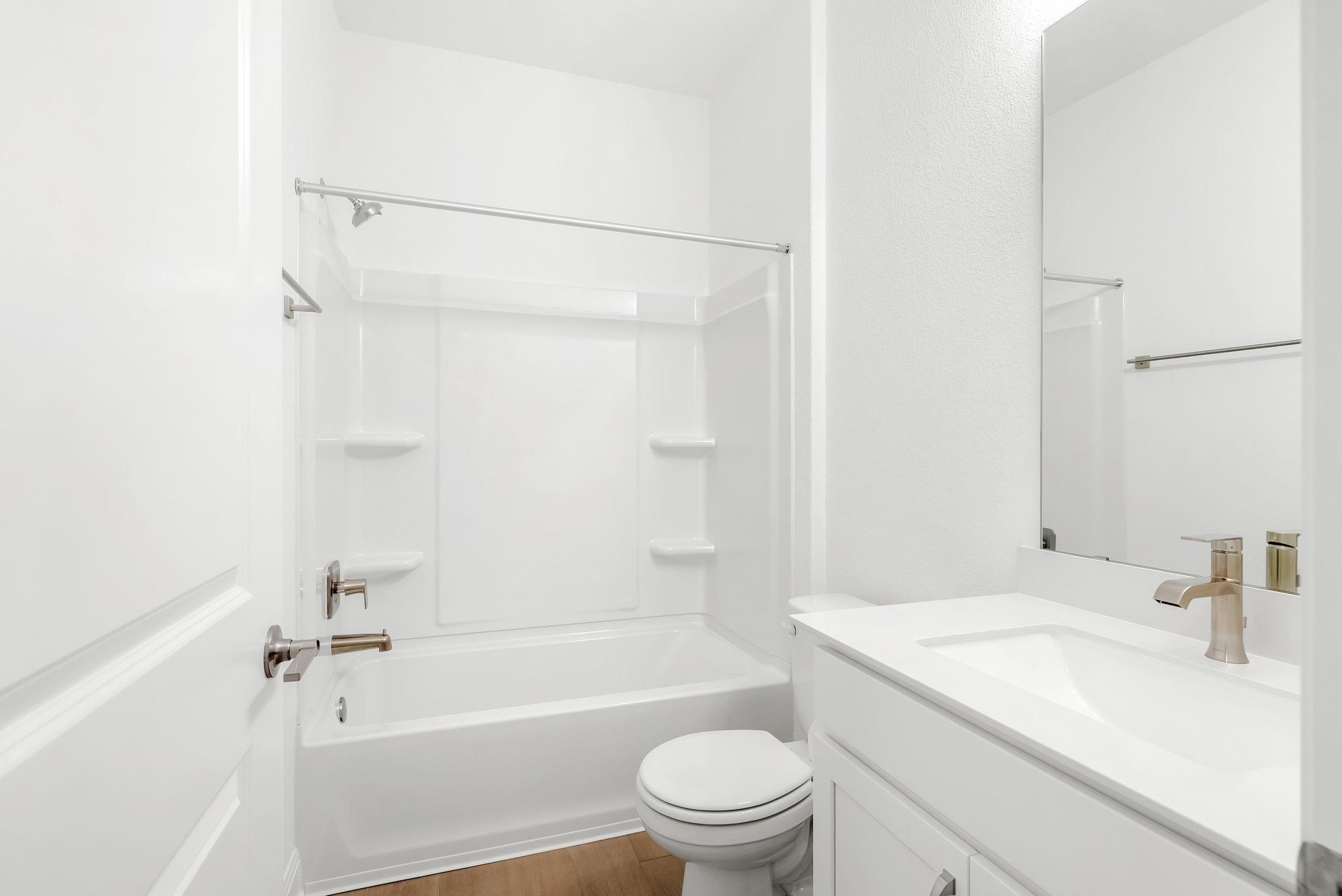 White bathroom with a tub-shower, toilet, and vanity beneath a large mirror.