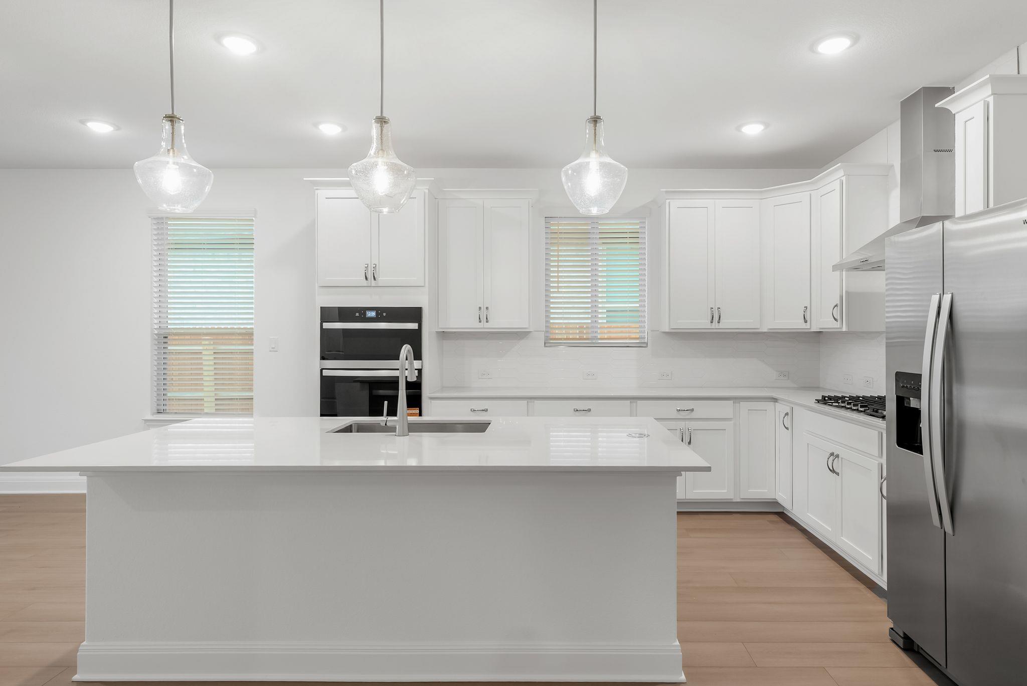 White kitchen with a large island, stainless steel appliances, and three pendant lights.