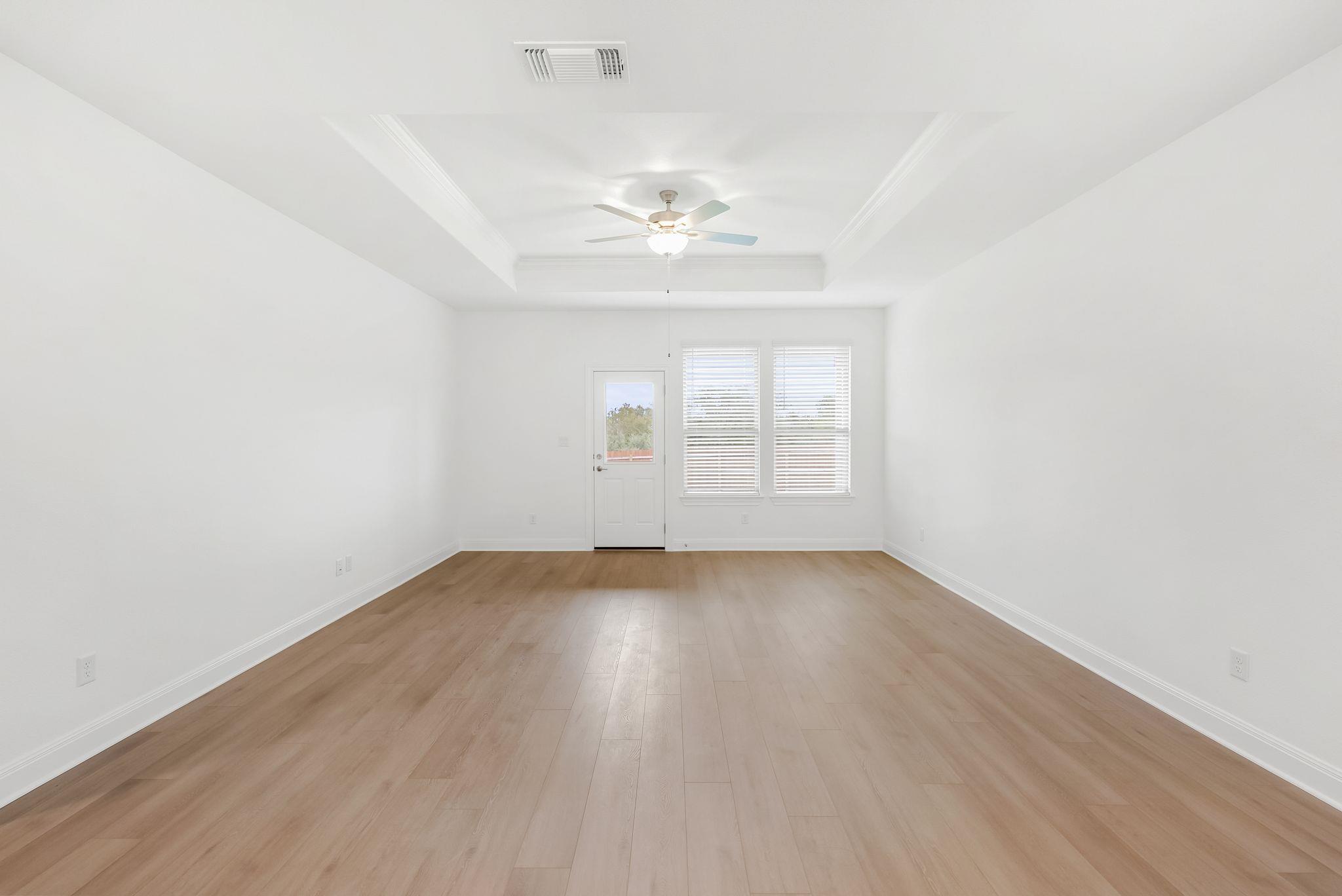 Empty room with light wood-look flooring, a tray ceiling, and a ceiling fan.