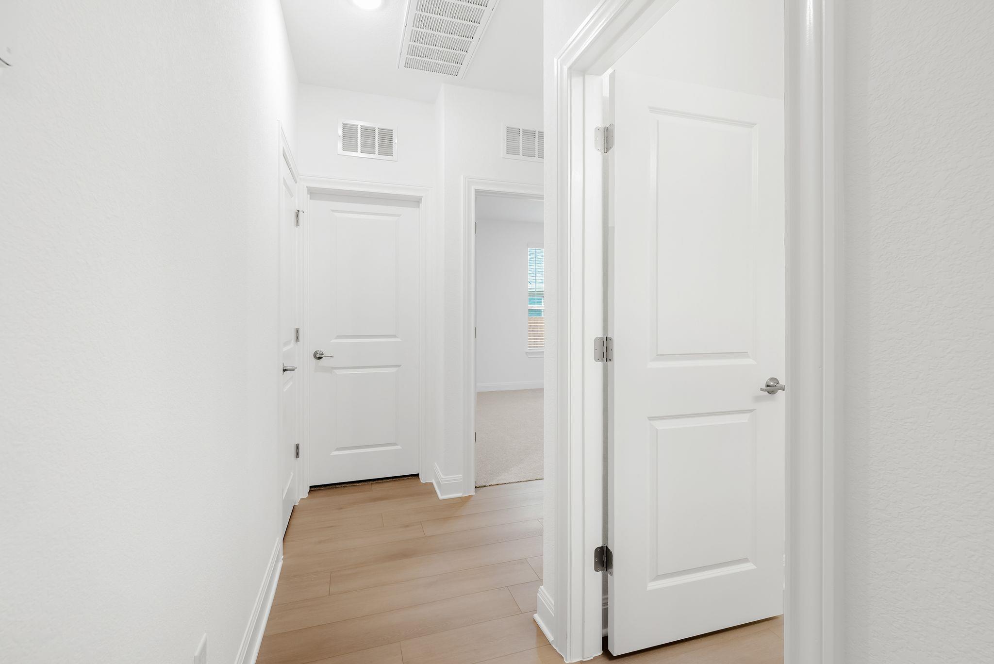 Empty hallway with light wood-look flooring and several white paneled doors.