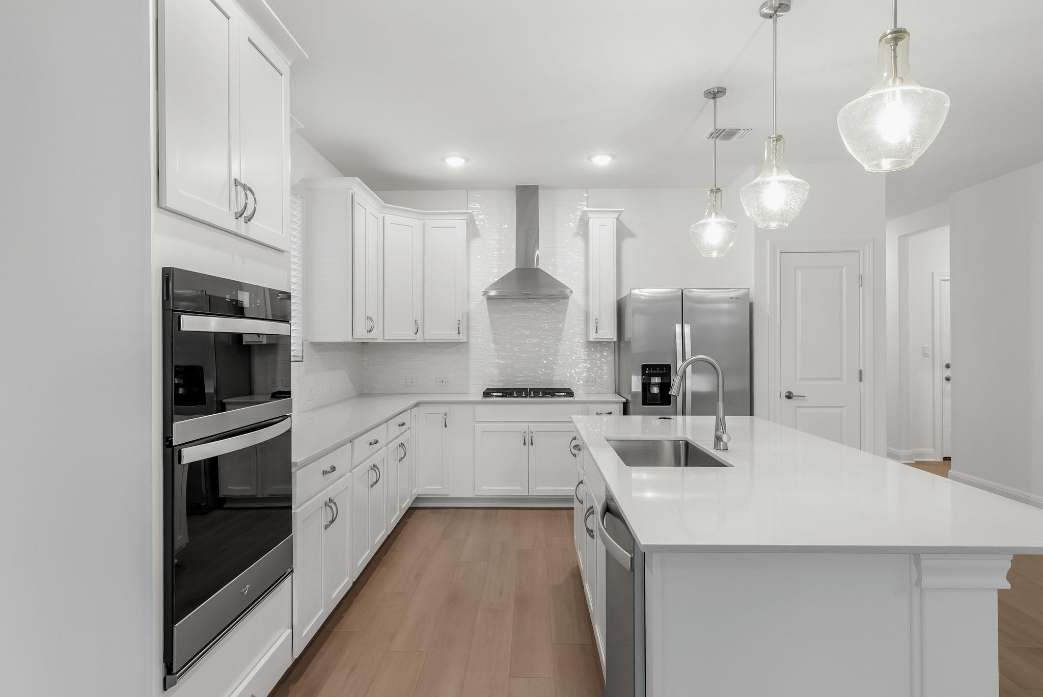 Modern white kitchen with a large island, stainless steel appliances, and glass pendant lights.