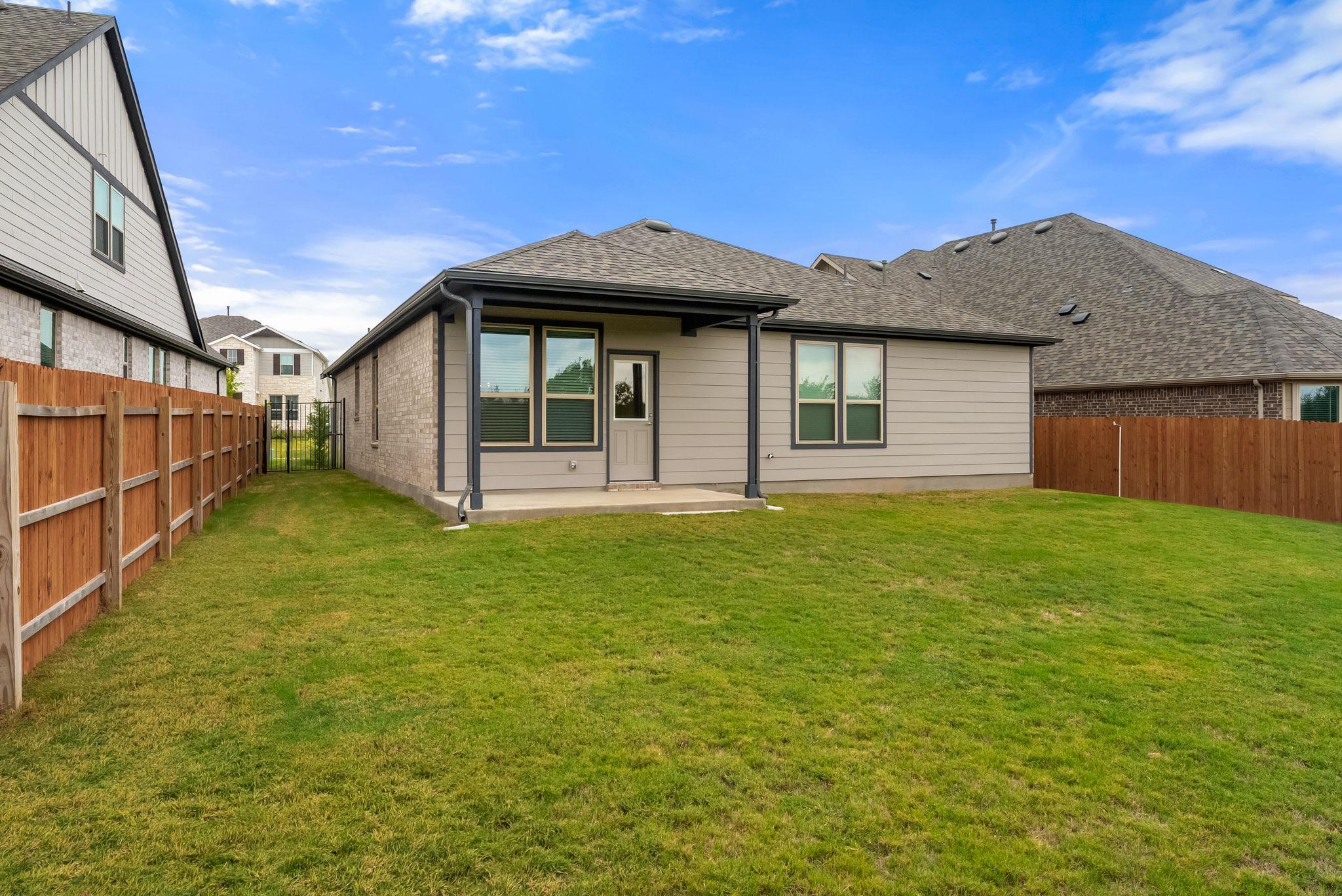 Rear exterior of a home with a covered patio, fenced lawn, and neighboring houses.