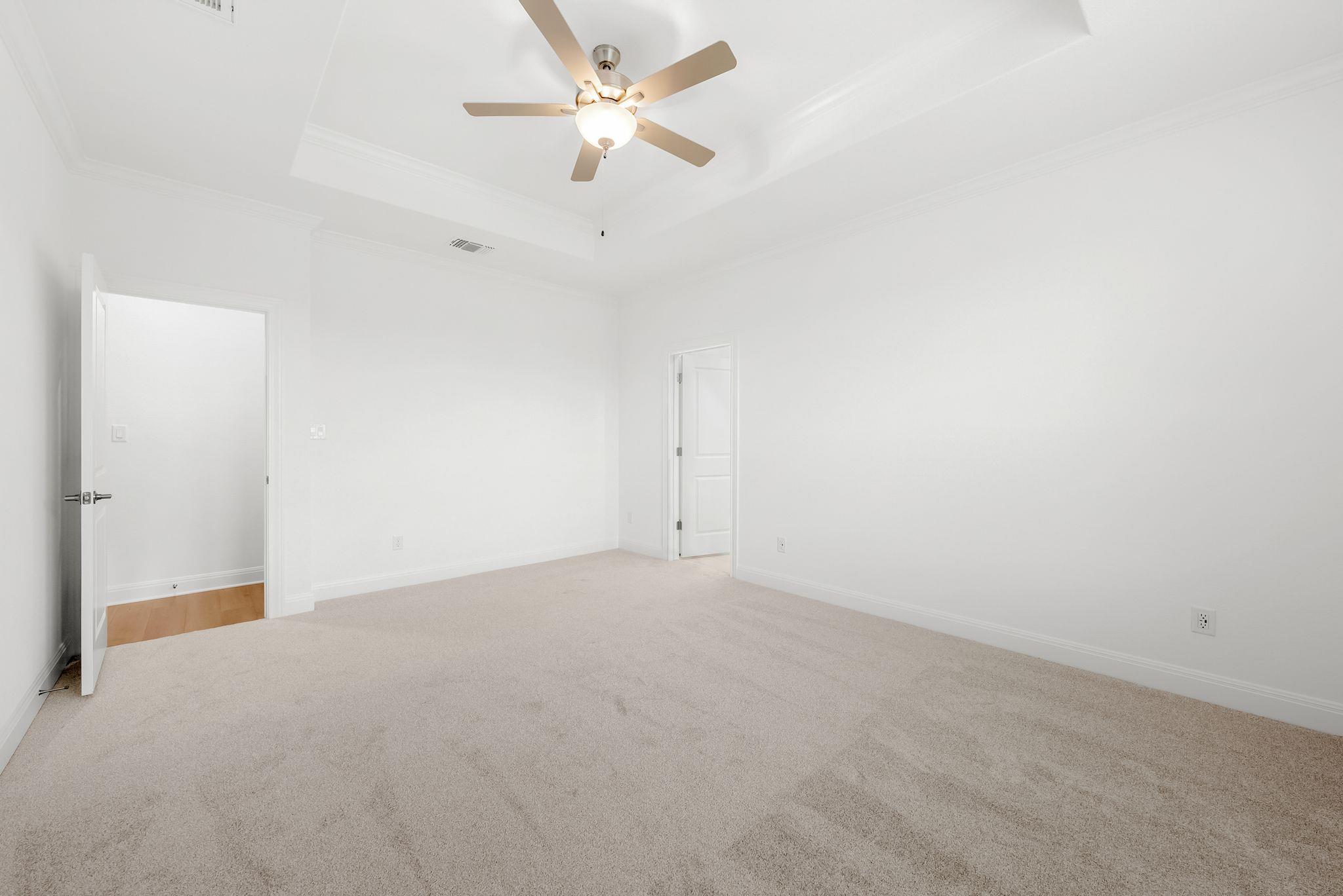 Empty carpeted bedroom with white walls, two doorways, and a ceiling fan with light.