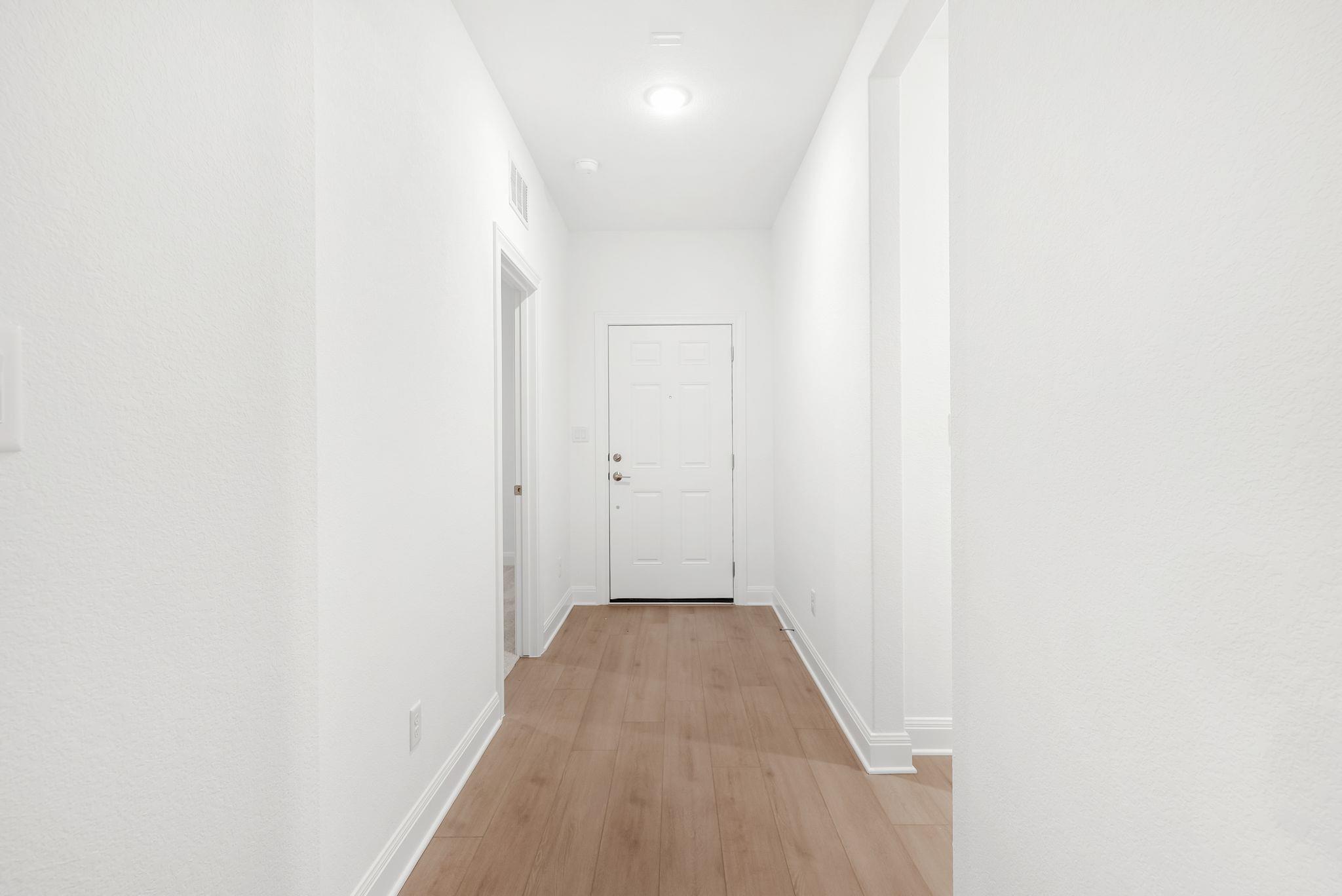 Unfurnished entry hall with light wood flooring and a white paneled front door.