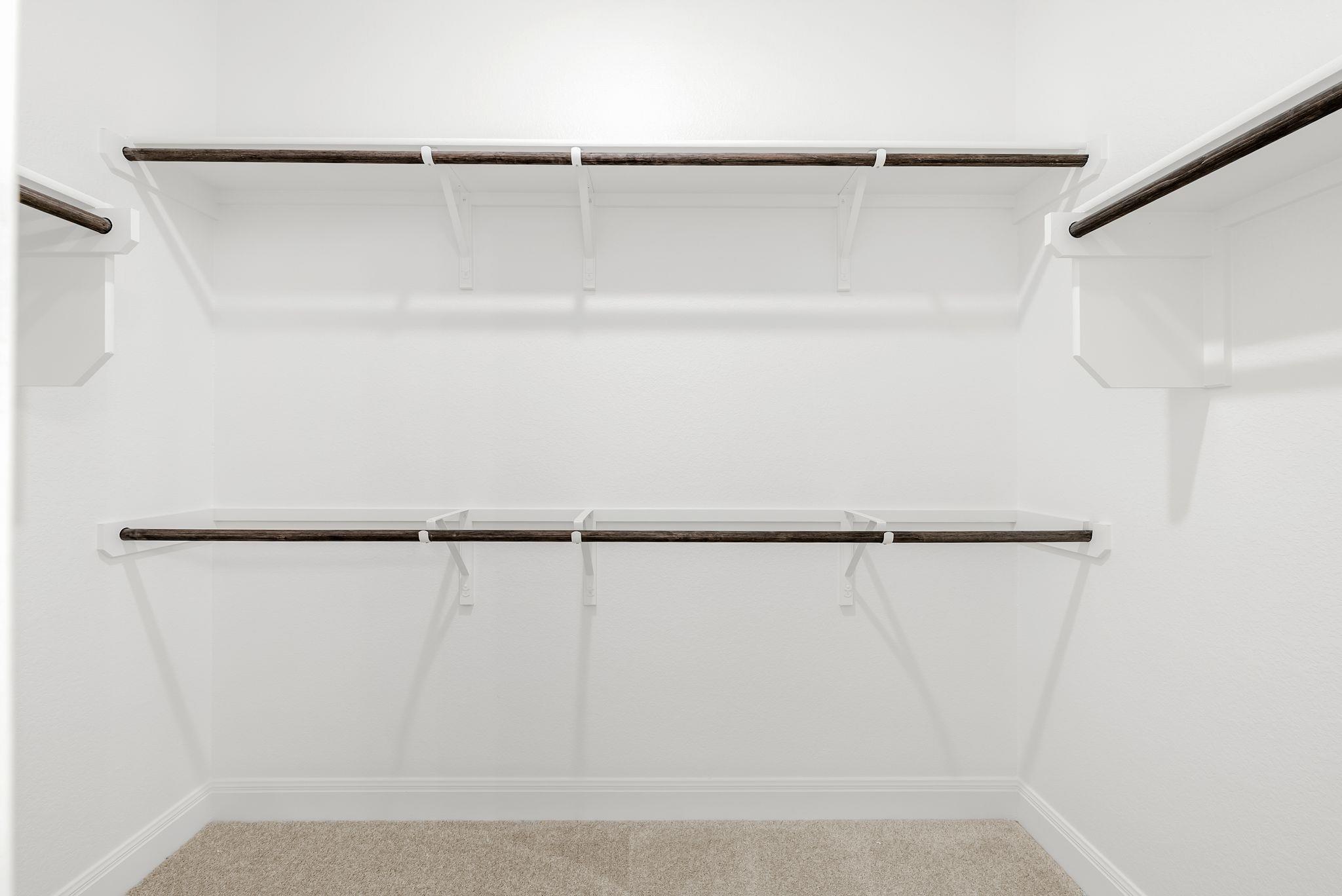 Empty white walk-in closet with dark wood hanging rods, built-in shelves, and beige carpet.
