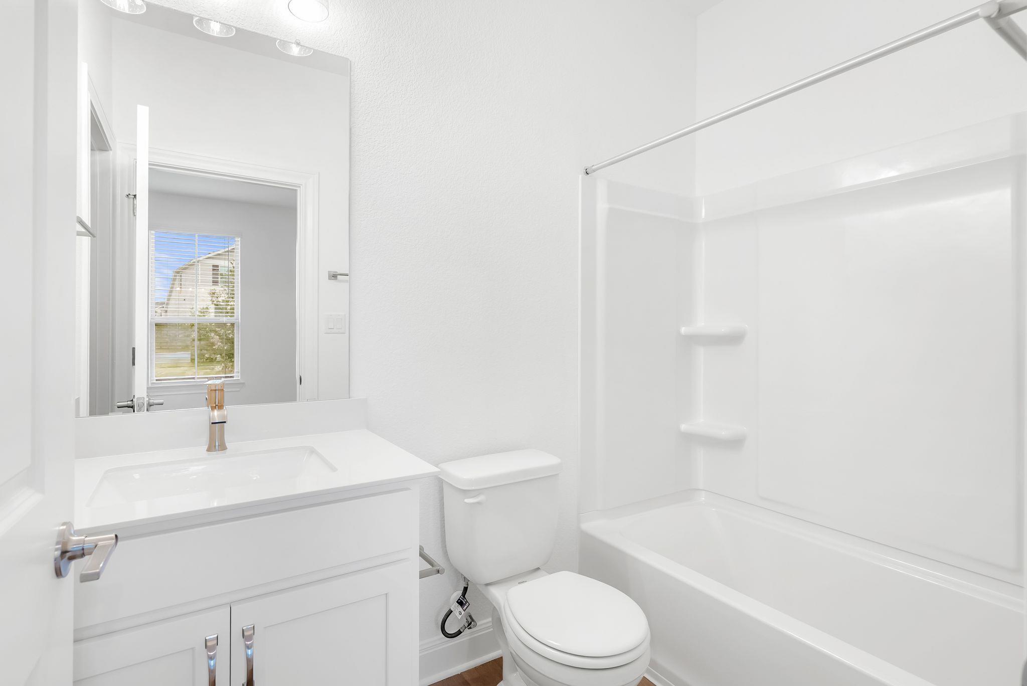 Bright bathroom with a white vanity, toilet, and tub-shower behind a clear glass enclosure.