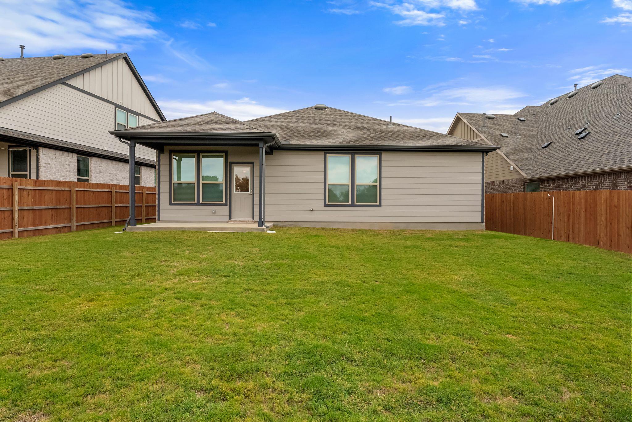 Rear of a single-story home with a covered entrance, fenced yard, and broad green lawn.