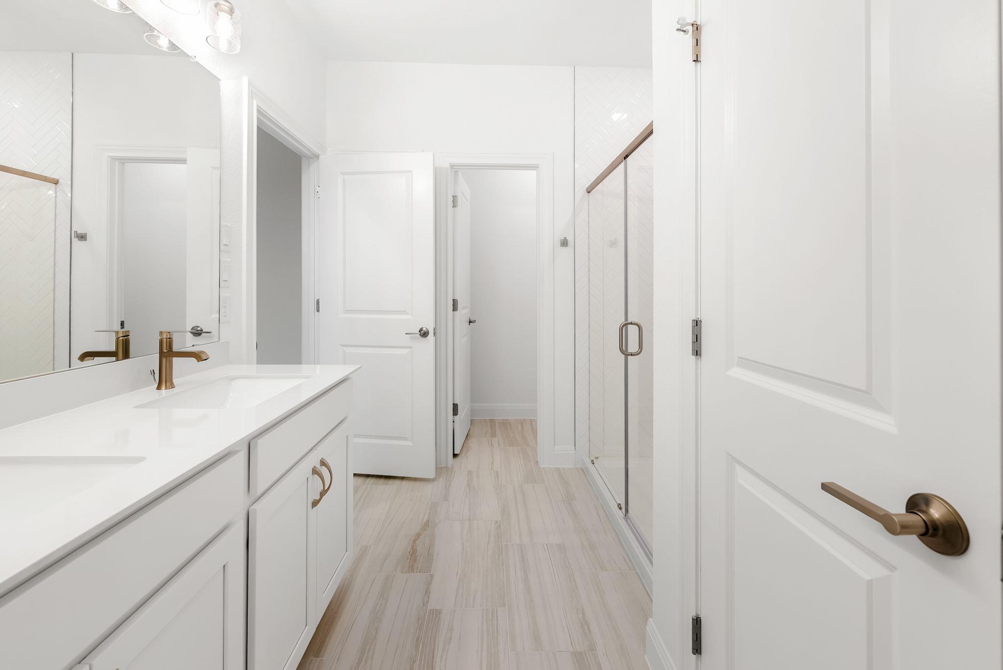 Bright bathroom with a white double vanity, brass fixtures, and a glass shower with herringbone tile.