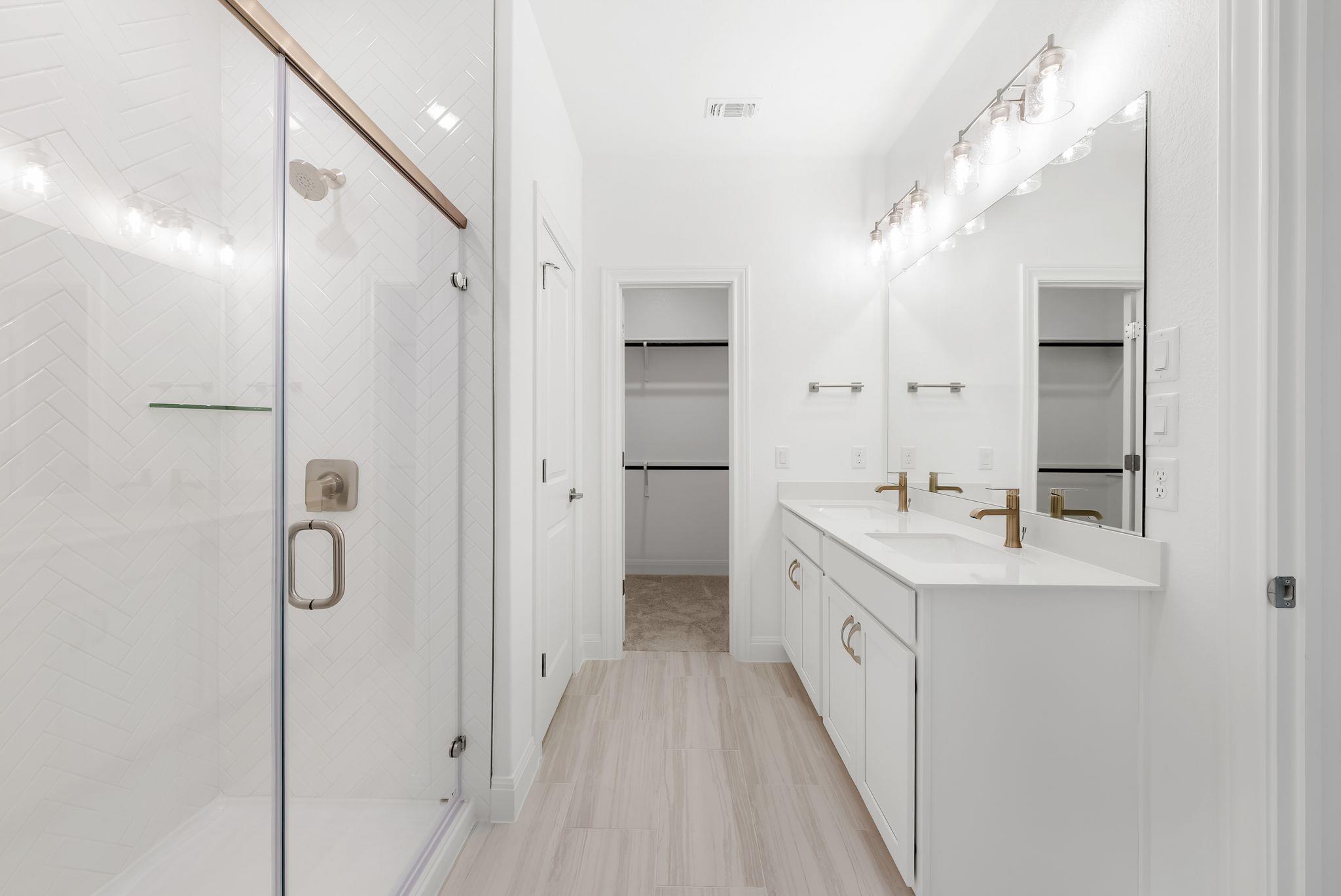 Bathroom with a white herringbone-tile shower and double vanity with gold-tone faucets.