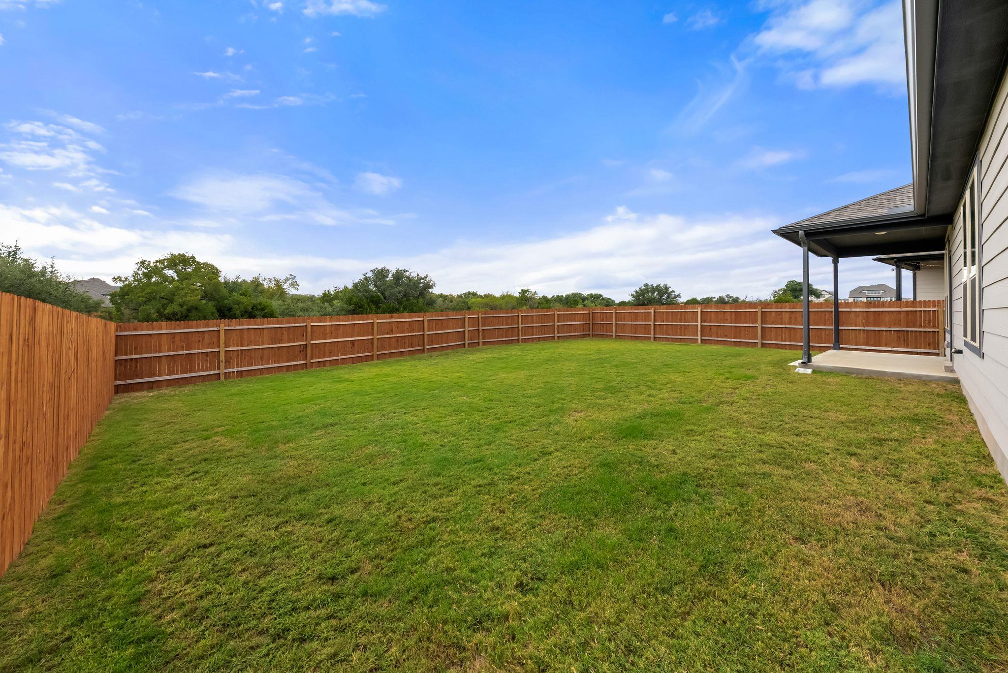 Fenced backyard with a broad lawn and covered patio beside the house.