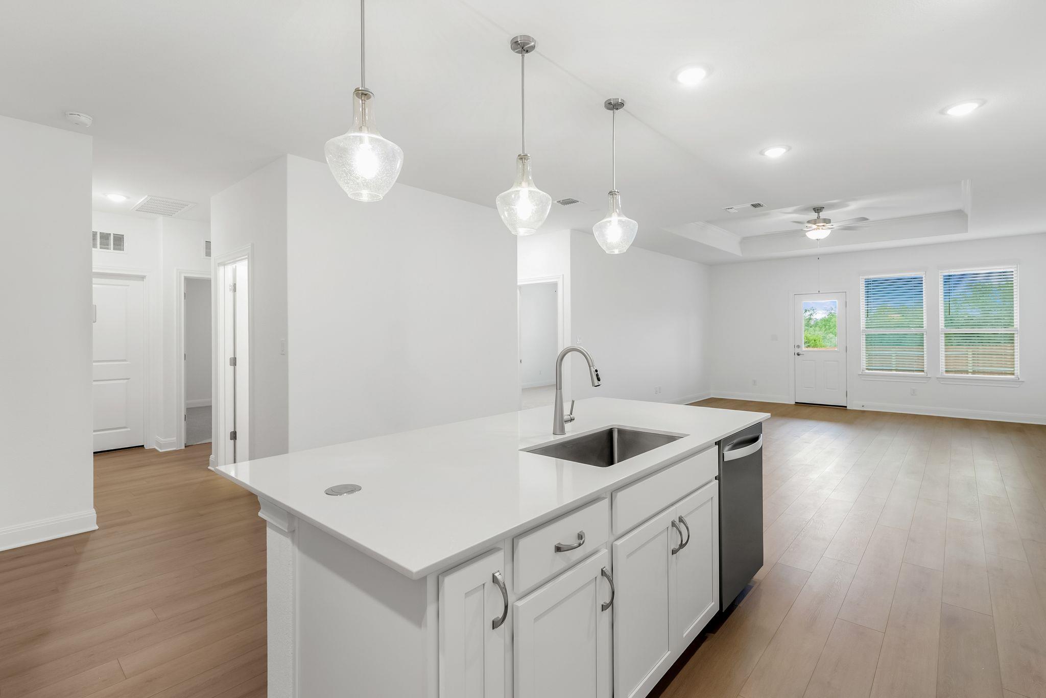 Vacant kitchen with a large white island and sink opening into a bright living area.