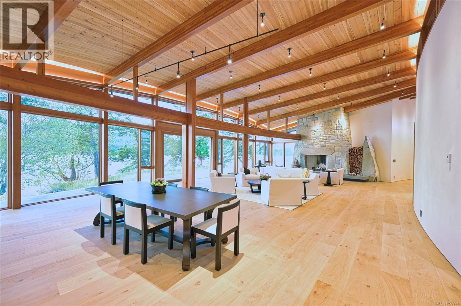Open-plan living and dining room with vaulted timber ceiling, stone fireplace, and water views through tall windows.