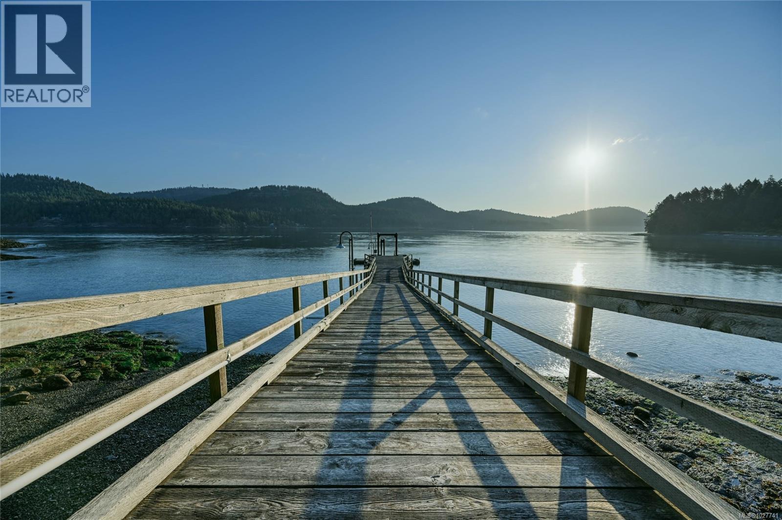 Wooden dock stretching into a calm bay, with wooded hills and low sun reflecting on the water.