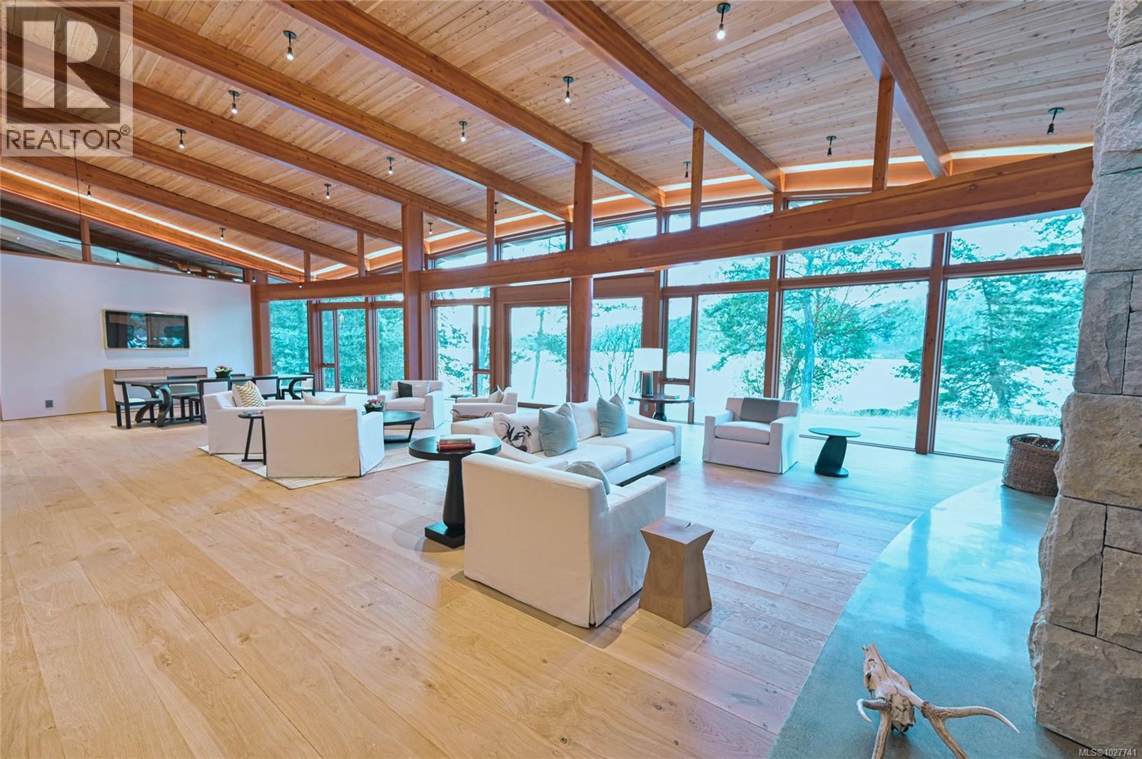 Waterfront living room with soaring timber ceiling, floor-to-ceiling windows, and white seating.