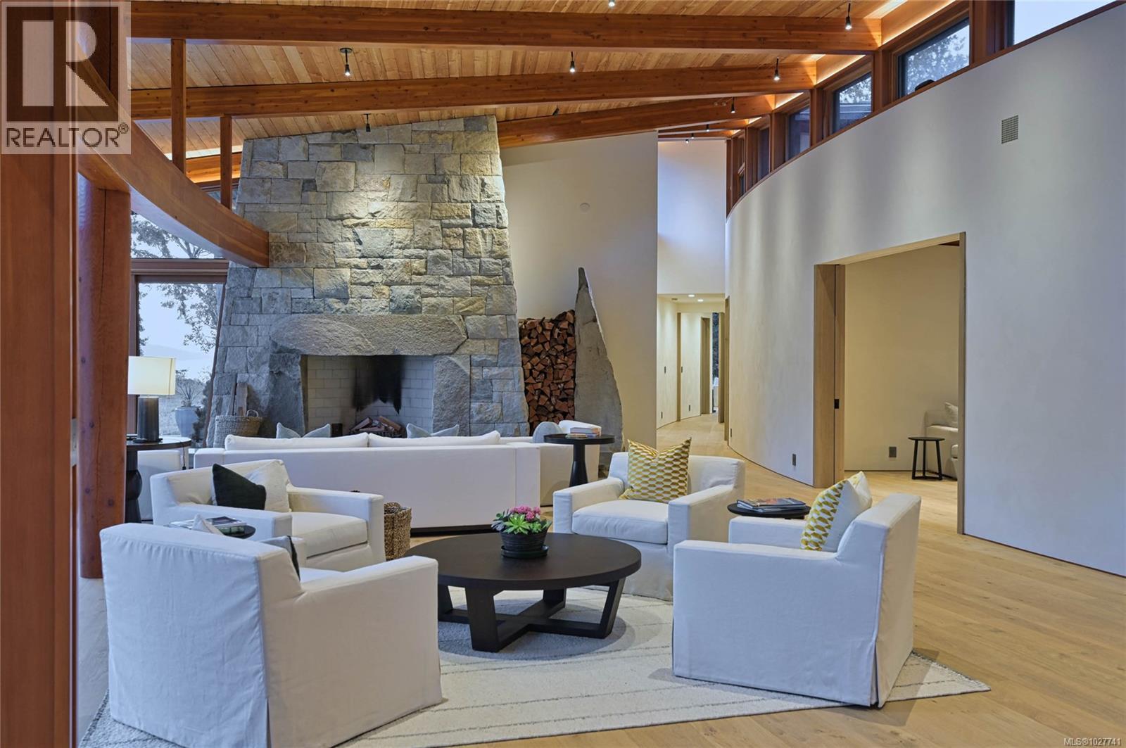 Living room with a massive stone fireplace, exposed timber ceiling, and white seating.