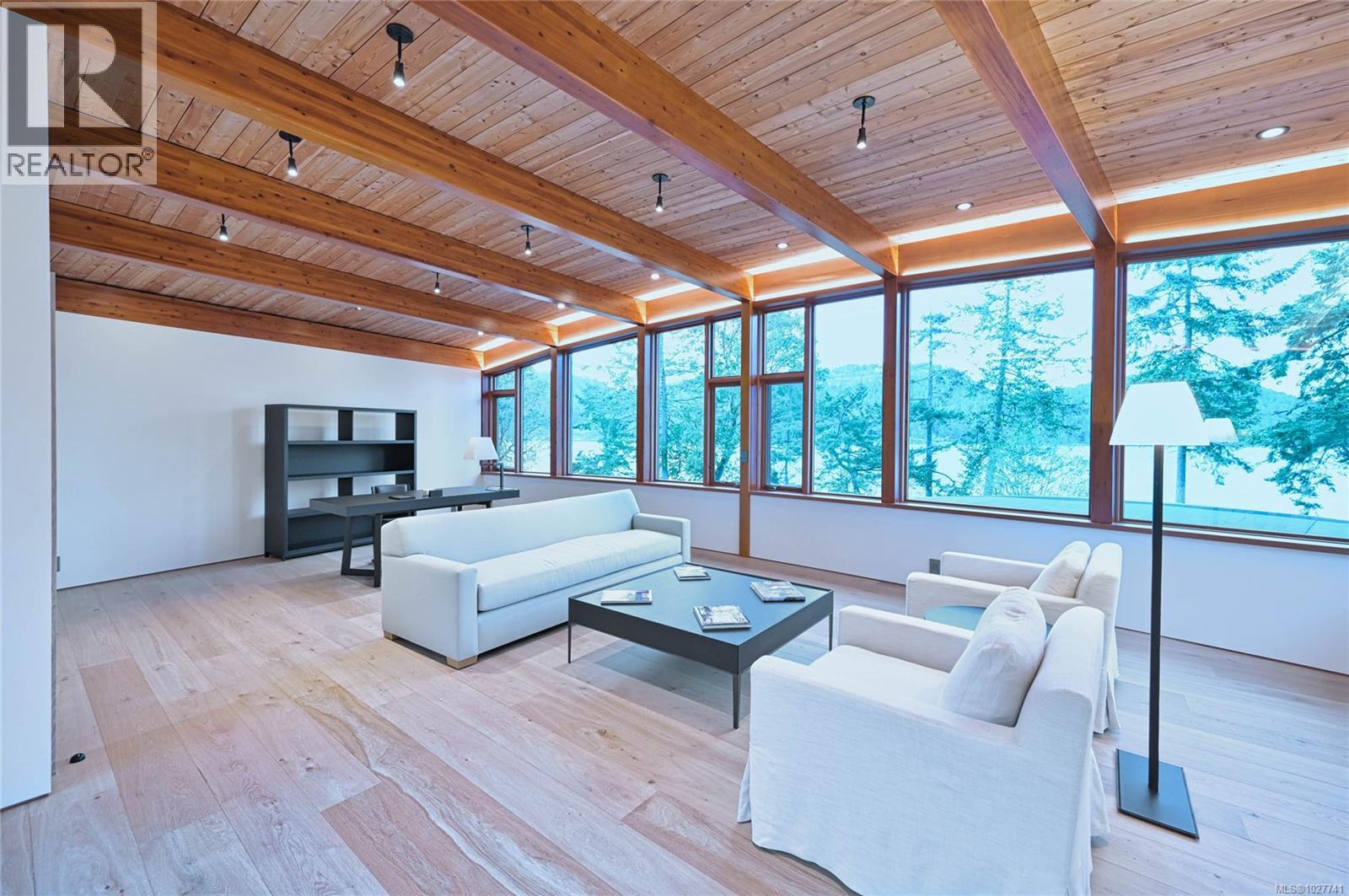 Living room with exposed timber beams, white sofas, and large windows overlooking water.