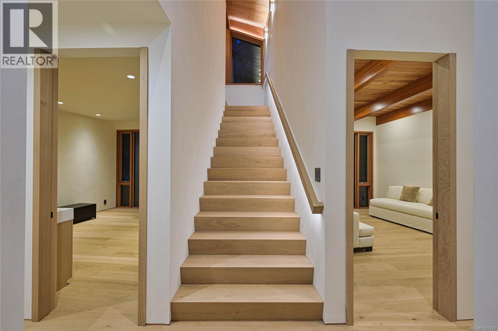 Light-wood staircase between two rooms, with matching floors and a timber-beamed ceiling.