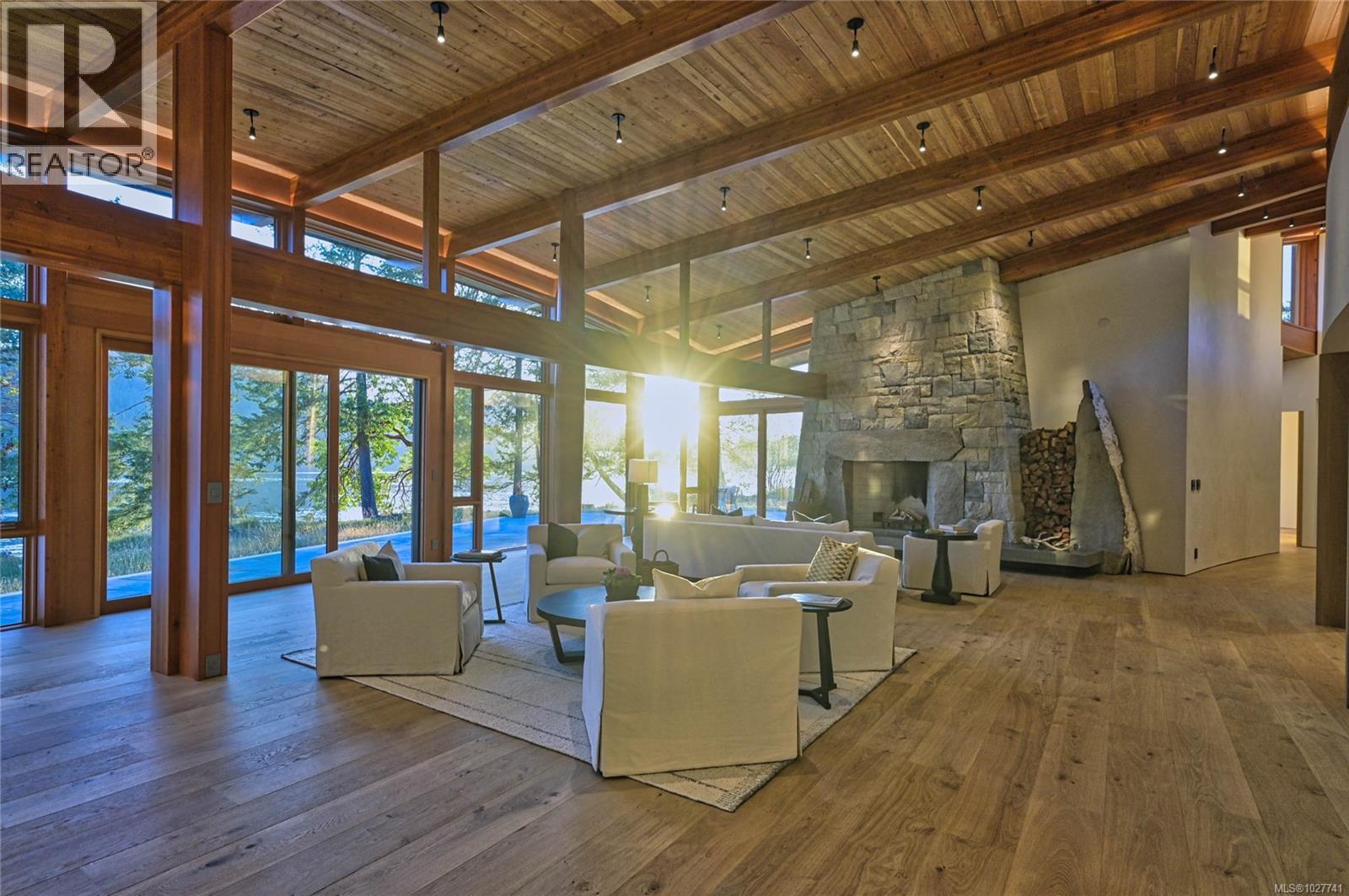 Living room with vaulted wood ceiling, stone fireplace, and windows overlooking the water.