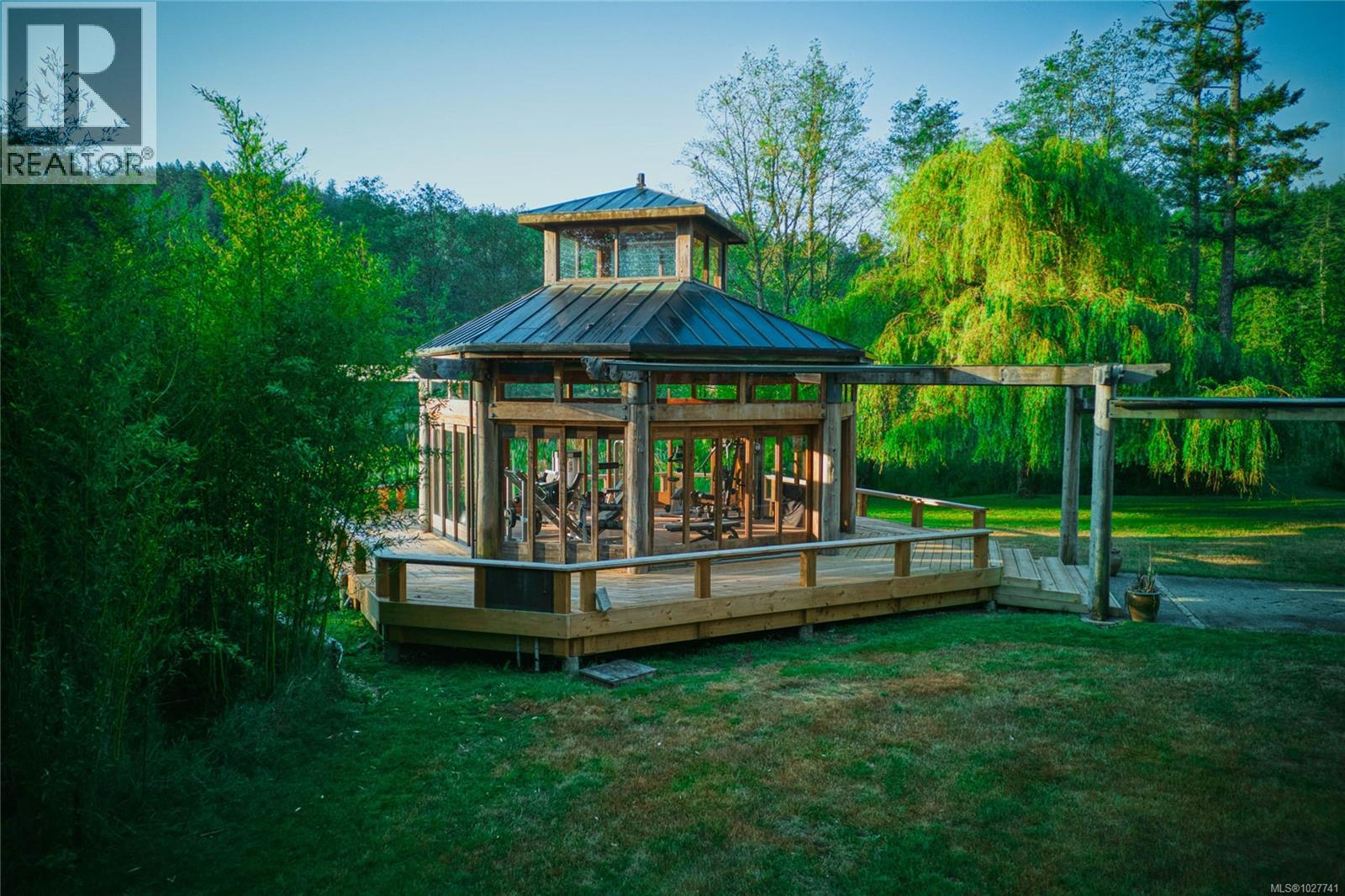 Glass-and-wood pavilion with a raised deck and pergola in a leafy yard.