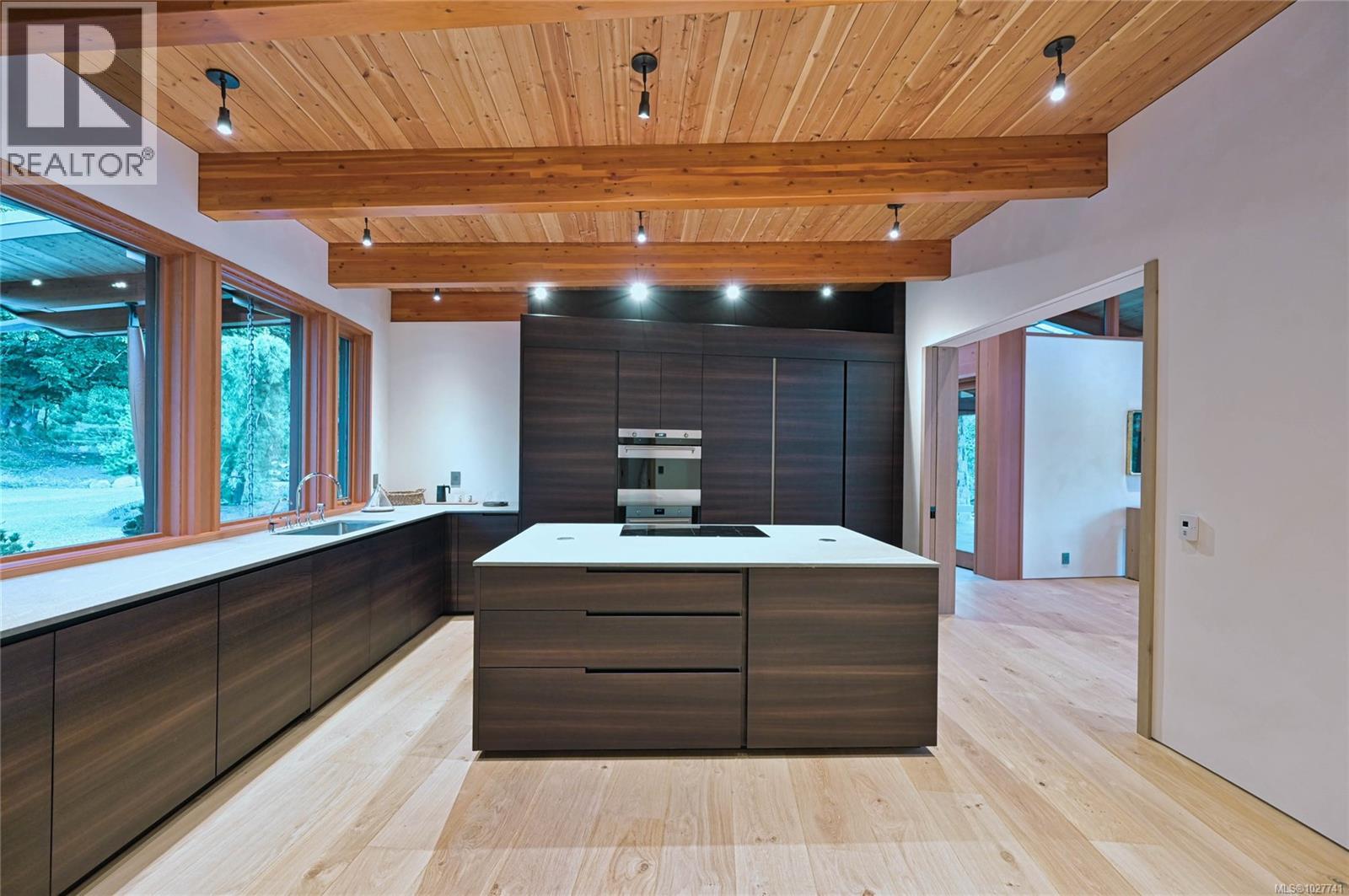 Modern kitchen with a large white island, dark cabinetry, and a beam ceiling.