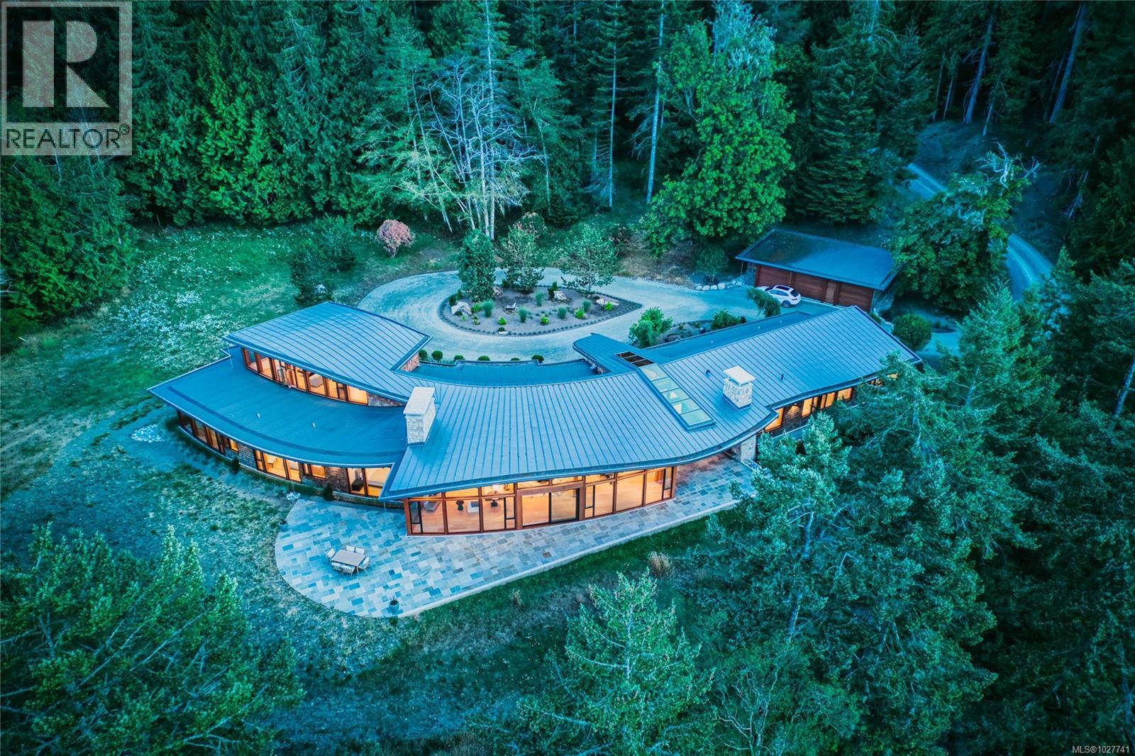 Aerial view of a modern home nestled in woodland, with a curved patio and circular driveway.