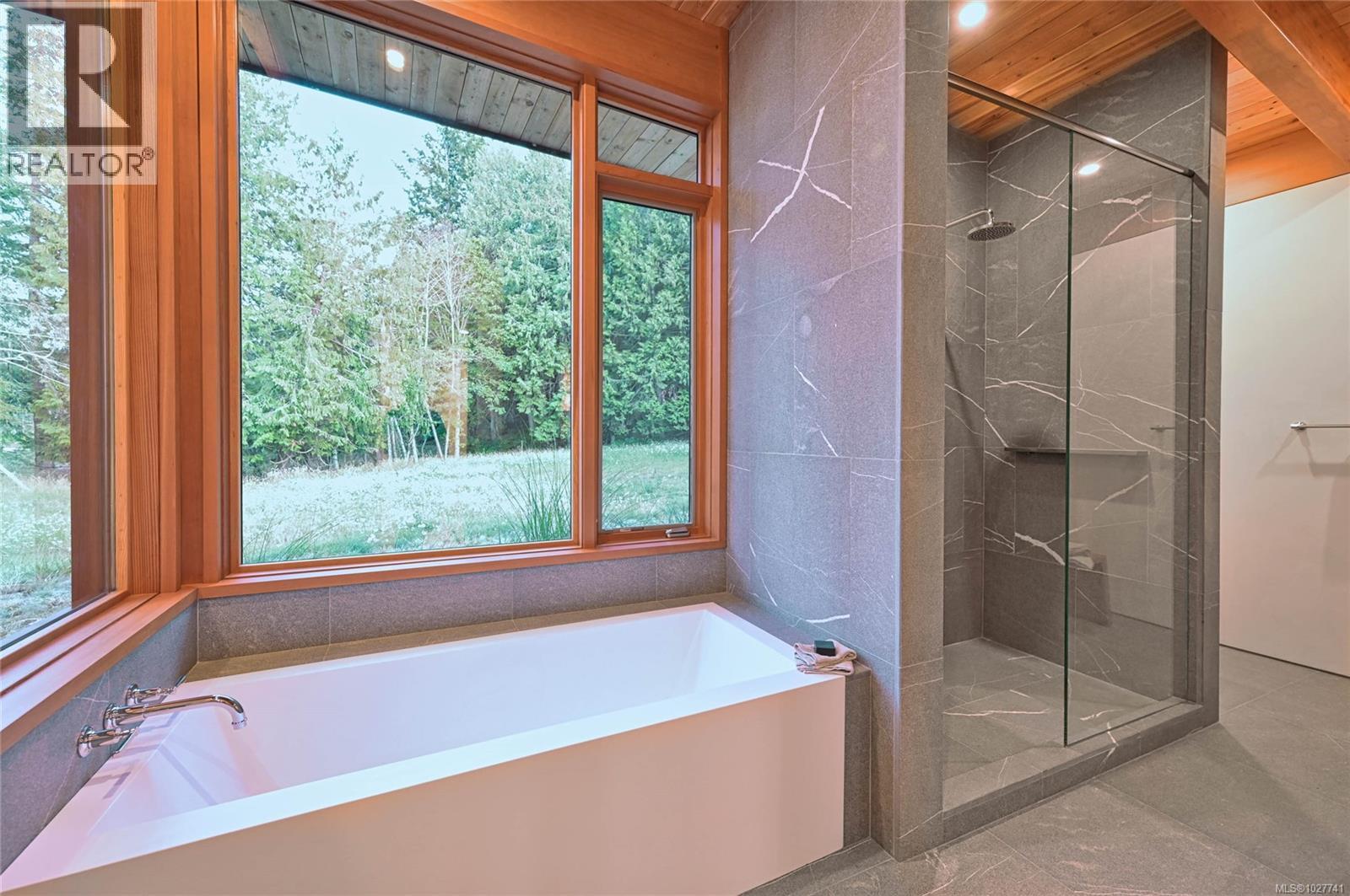 Modern bathroom with a freestanding tub, glass shower, and large windows overlooking greenery.