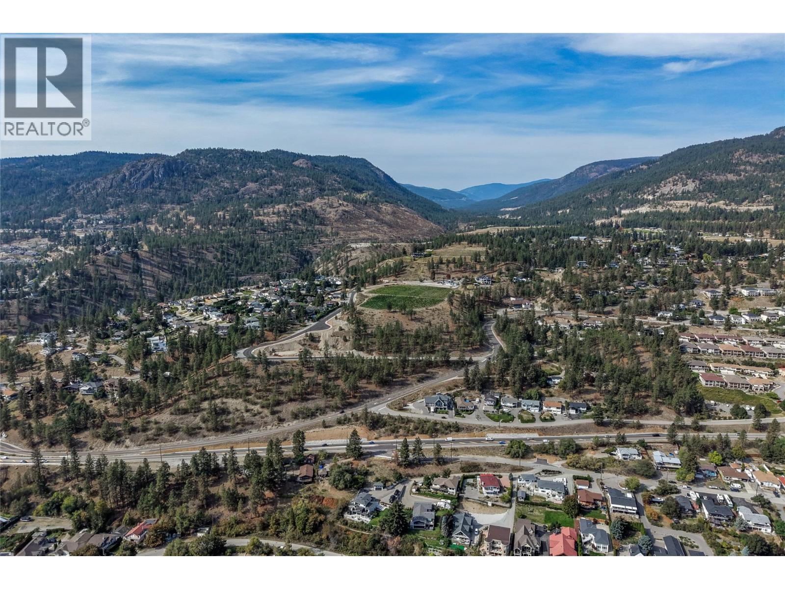 Aerial view of a residential valley neighborhood with winding roads and forested mountains.