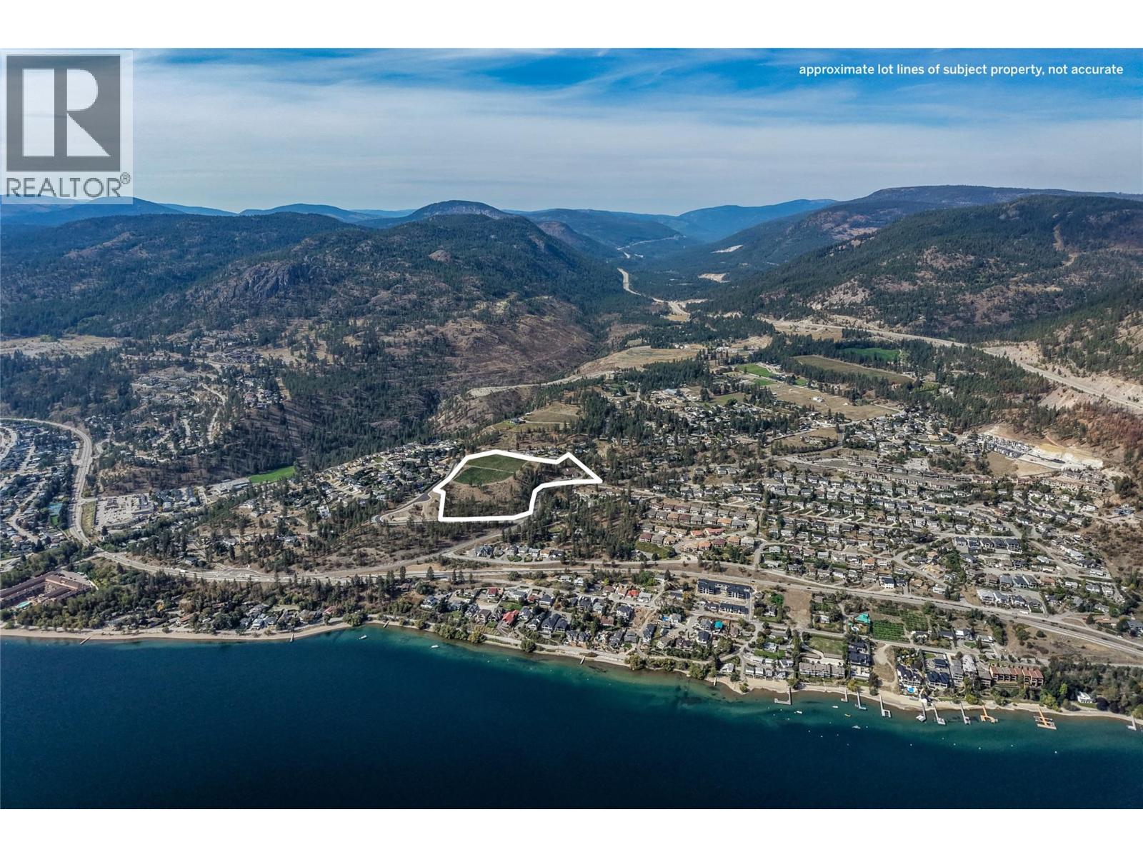 Aerial view of a lakeside town, forested mountains, and a white outline marking a land parcel.