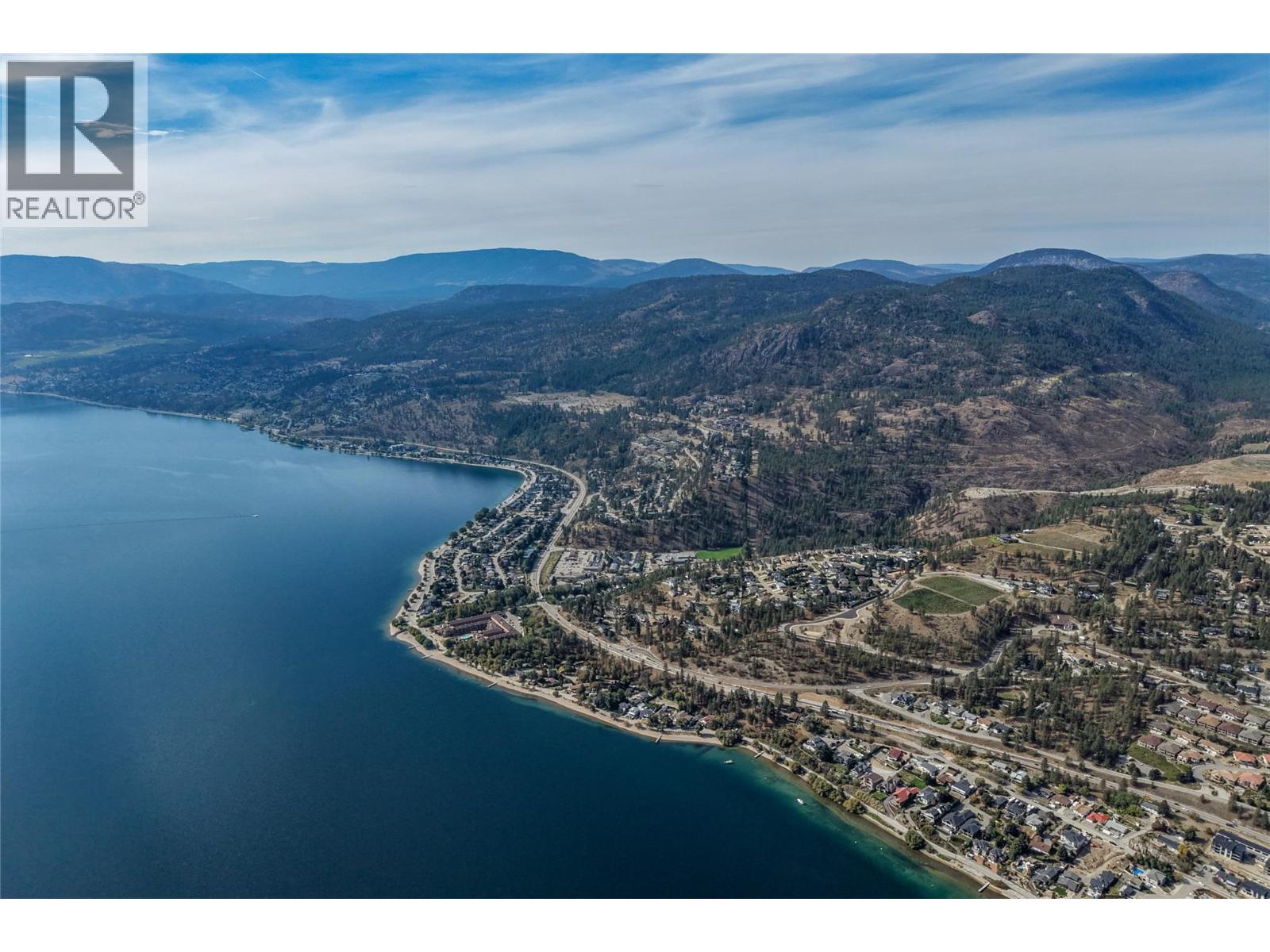 Aerial view of Peachland’s shoreline, with Okanagan Lake, homes, and wooded mountains.