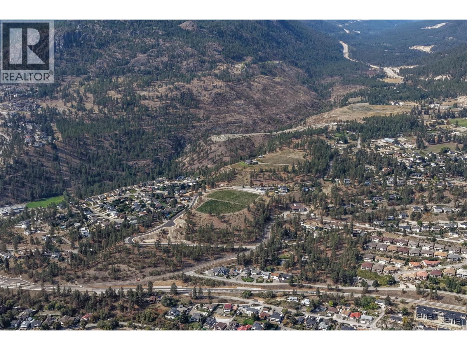 Aerial view of a Peachland neighborhood beneath dry, forested hills and winding roads.