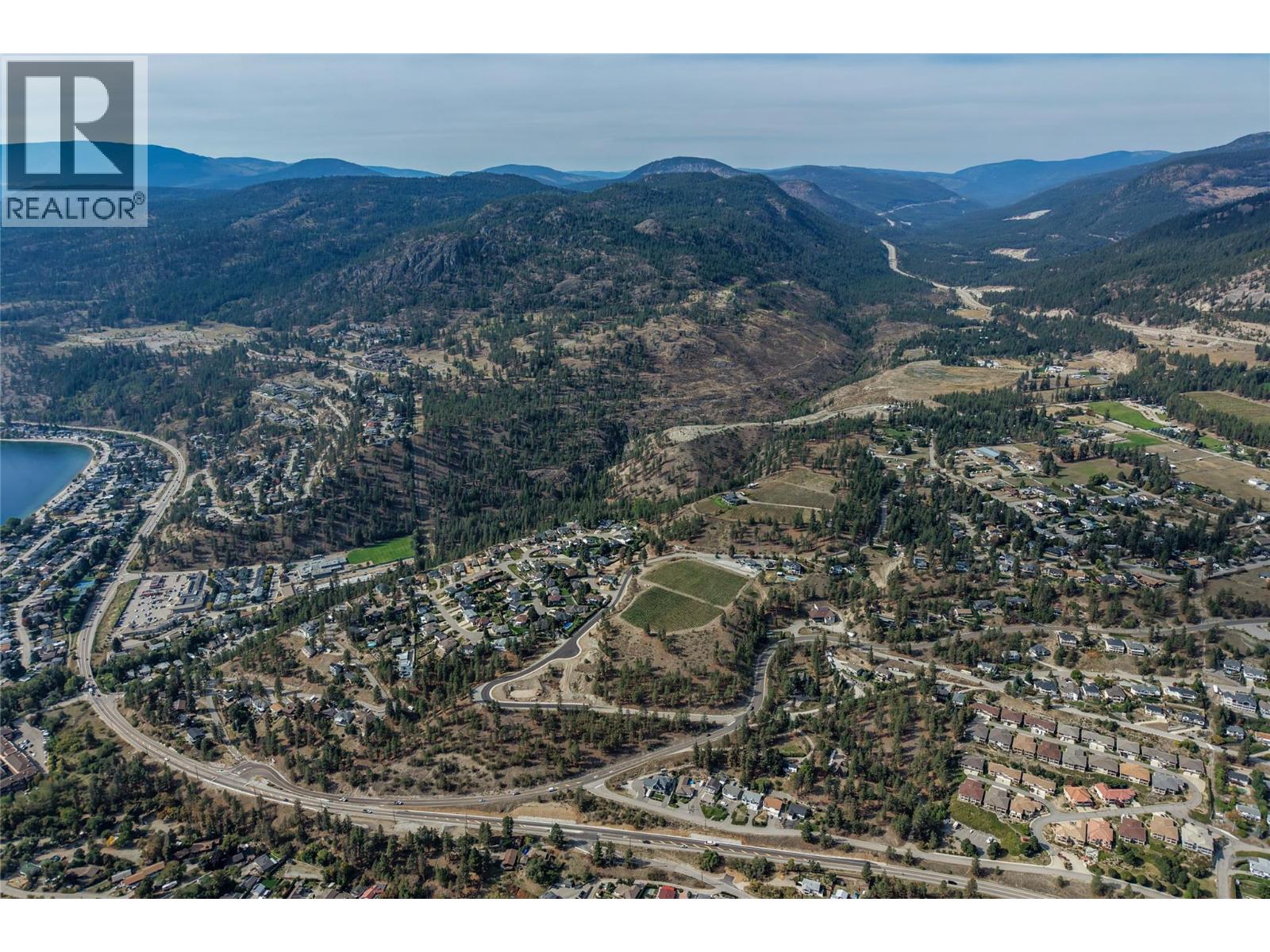 Aerial view of homes and roads near a lake, with forested hills and a valley in the distance.