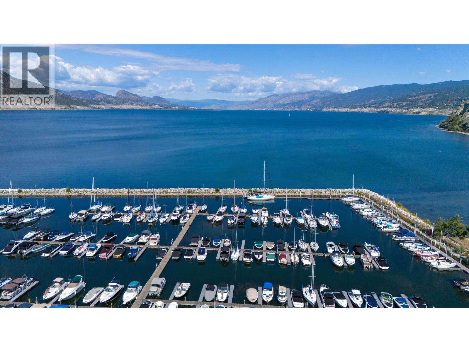 Marina crowded with boats beside a blue lake, with mountain ranges across the water.