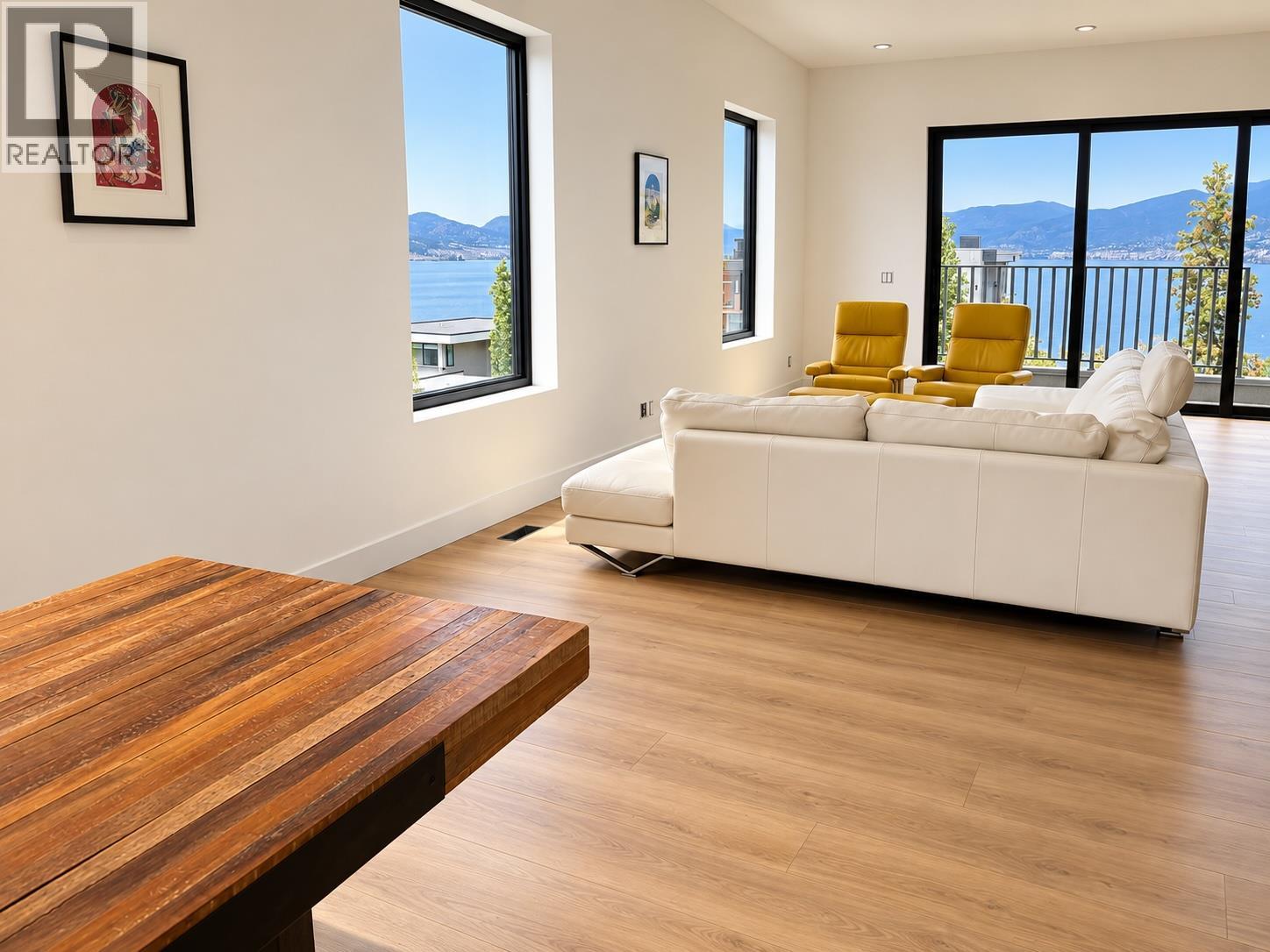 Living room with a white sectional and yellow chairs overlooking a lake and mountains.