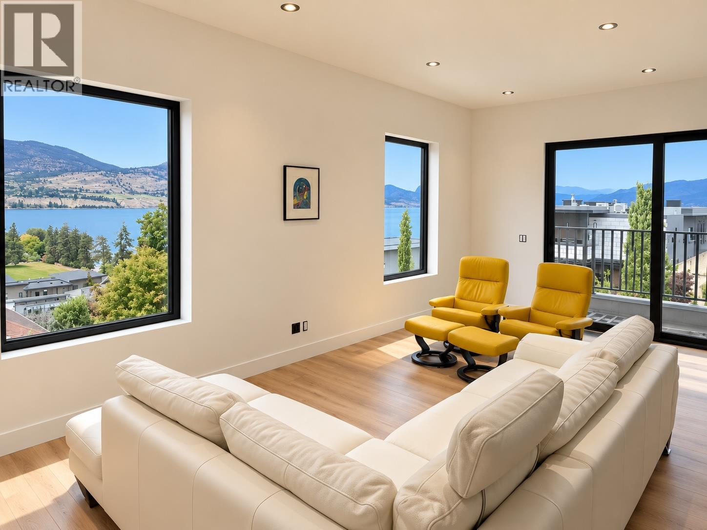 Furnished living room with yellow lounge chairs and wide lake and mountain views through large windows.