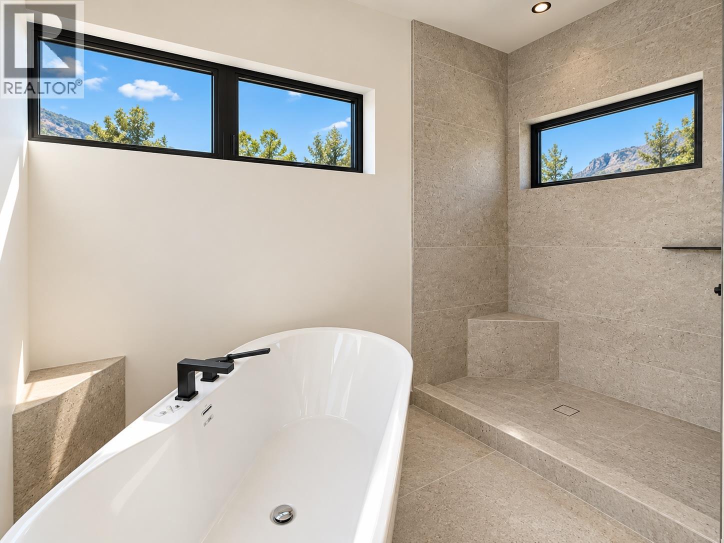 Modern bathroom with a freestanding tub, tiled walk-in shower, and windows overlooking a mountain.