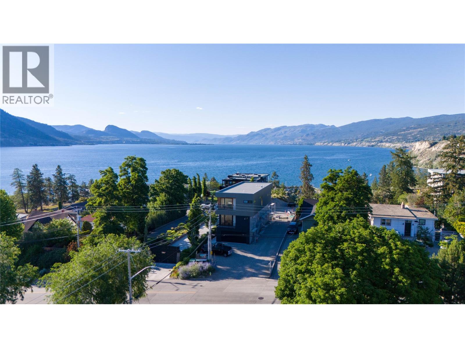 Lakeside neighborhood with homes and trees in the foreground, blue water and mountain ranges beyond.
