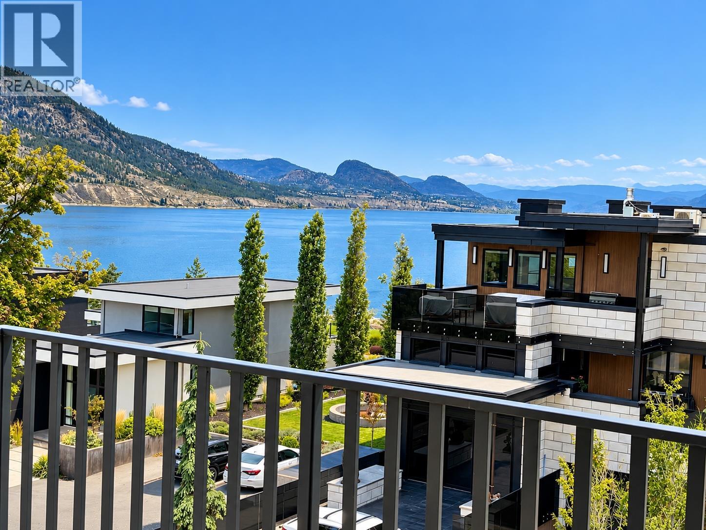 Modern homes overlooking a lake and mountains, seen from an elevated balcony.