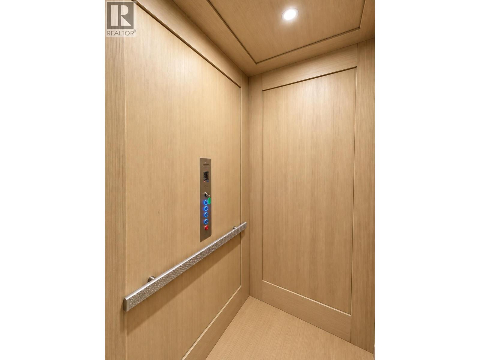 Wood-paneled elevator interior with illuminated controls and a metal handrail.