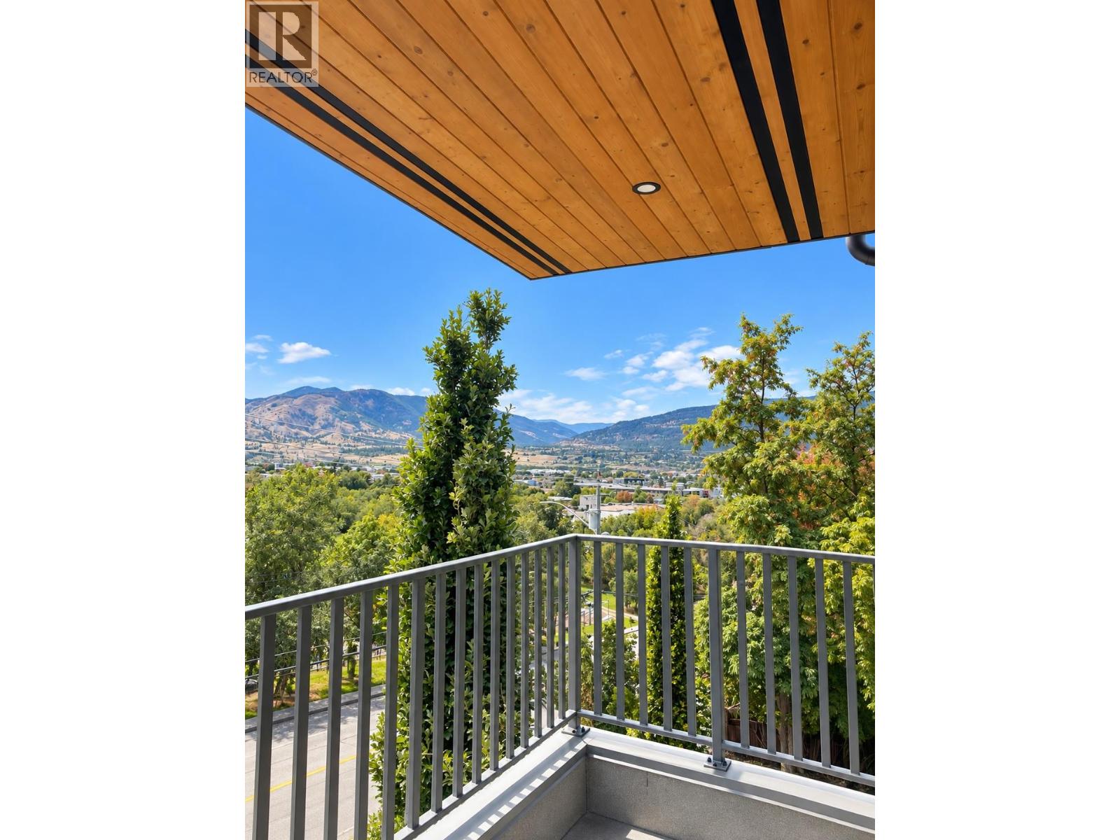 Balcony with a wood soffit and metal railing overlooking a leafy valley and mountains.