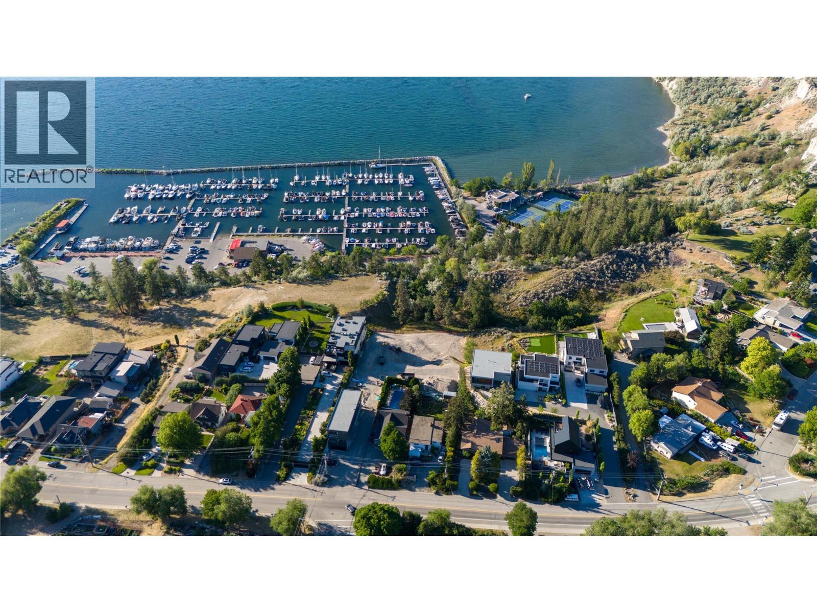 Aerial view of a lakeside marina and nearby homes, with boats and tennis courts.